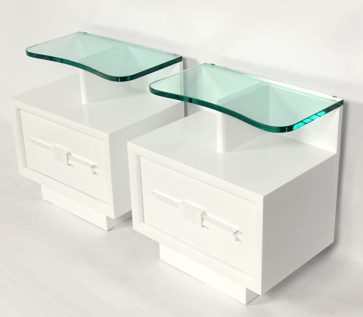 Pair of glamorous white lacquer and glass nightstands, American, circa 1930s. They have been refinished and are ready to use. They each feature a low maintenance glass top with a shelf underneath, and a deep drawer at the bottom. They are a