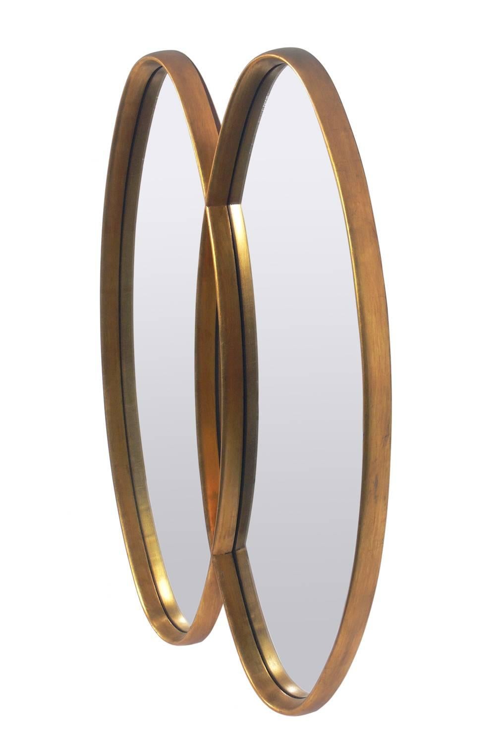 Modernist oval gold leaf double mirror, American, circa 1960s. It exhibits wonderful patina and wear to the gold leafing, beautifully exposing a bit of the Chinese red bole or underlayer. This mirror has a sculptural form and would fit seamlessly