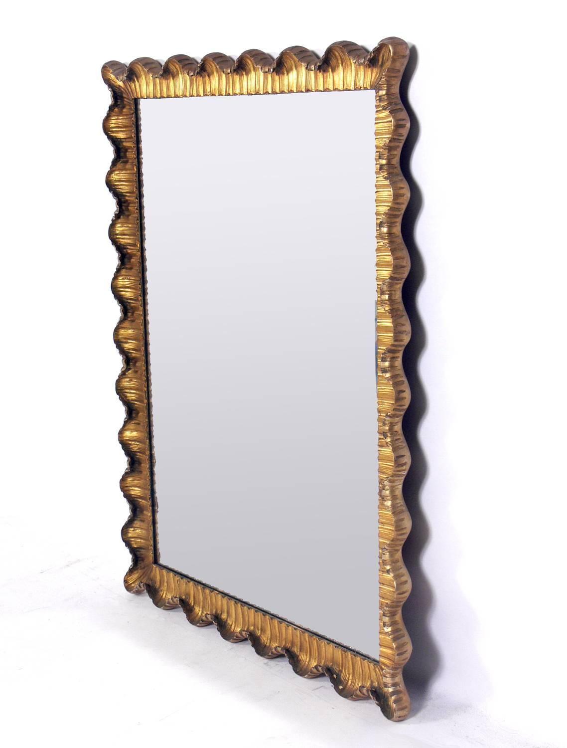 Venetian scalloped mirror, Italy, circa 1950s. Gold leaf gilt in the front and silver leaf gilt on the sides and back of the frame. Undulating curves of hand-carved and giltwood and gesso give this mirror its elegant form. The original gilt finish