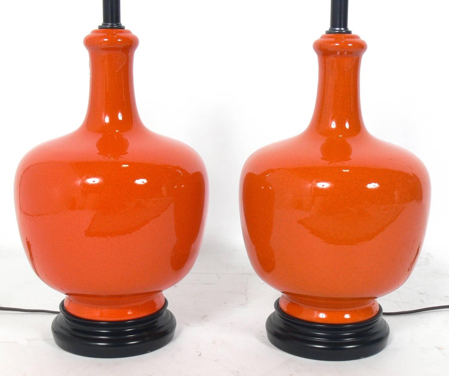 Pair of vibrant orange ceramic lamps, American, circa 1950s. They have a subtle Asian influence and the vibrant orange ceramic bodies exhibit beautiful craquelure. Rewired. The price noted below includes the shades.