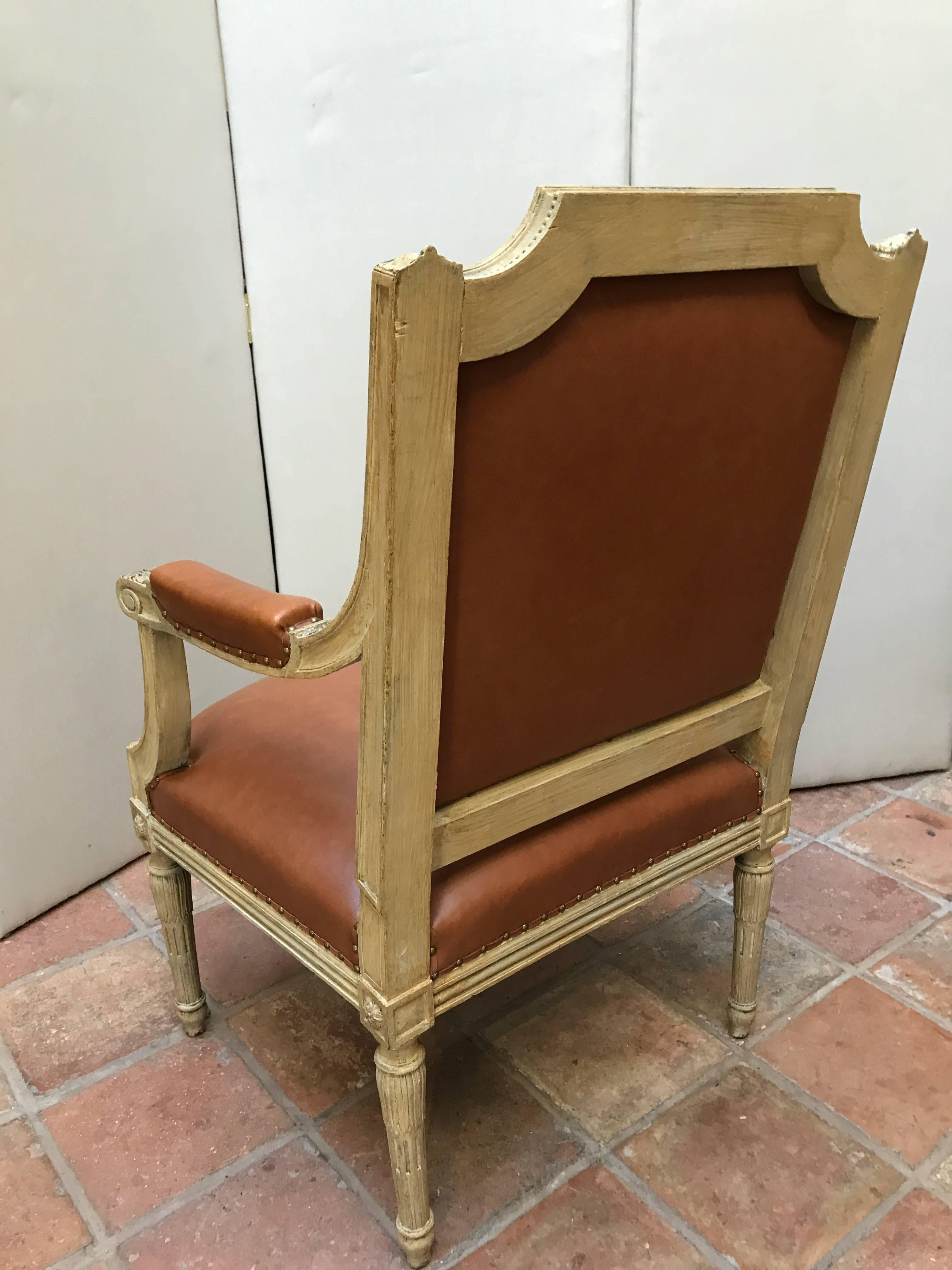 A fine set of four 19th century Louis XVI style Fauteuils (wooden armchairs) with generous proportions and intricately carved neoclassical decoration. These beautiful chairs retain their old painted finish with contemporary brown leather upholstery.