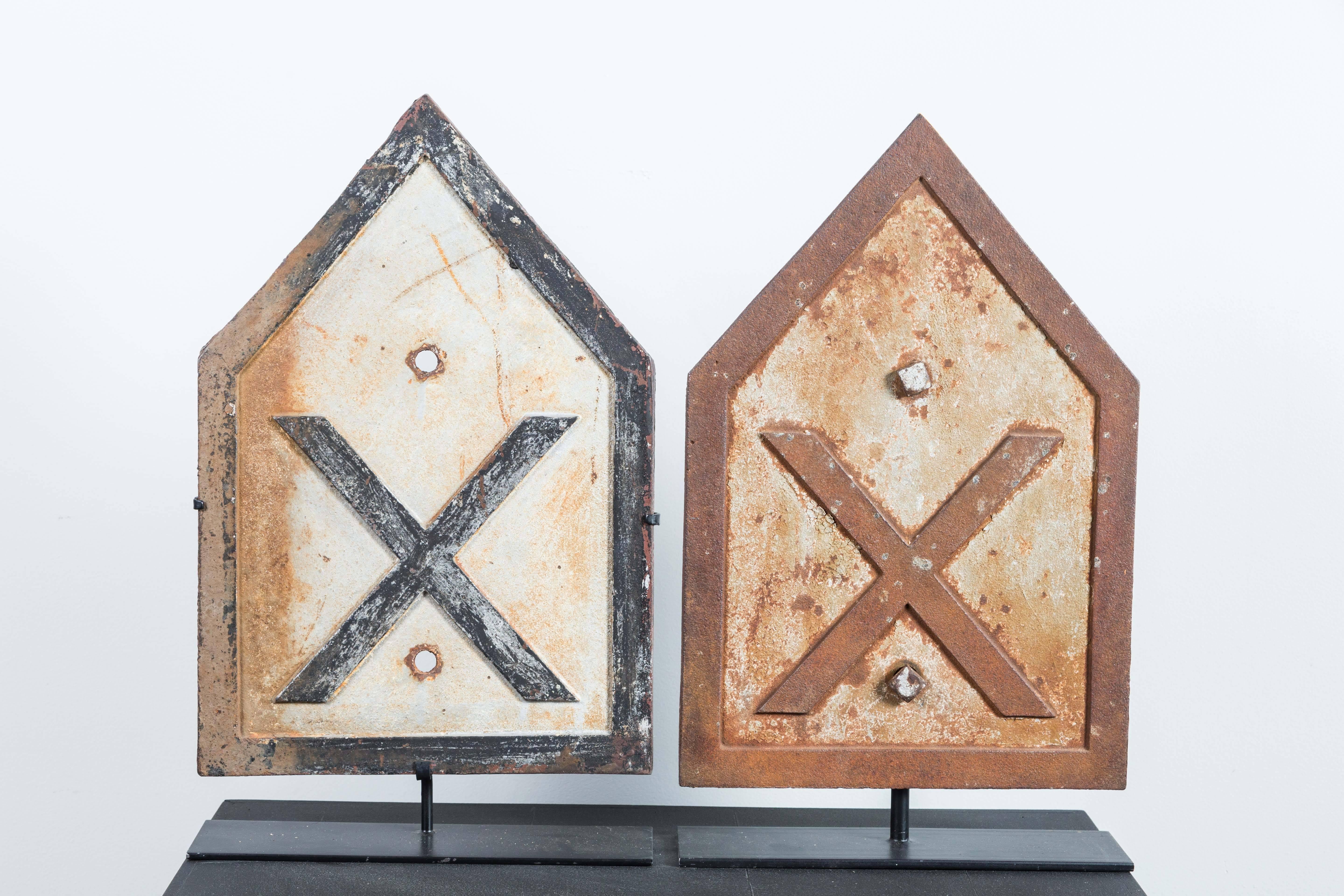 Collection of three iron railroad crossing "X" signs. Three dimensional lettering with different original paint surfaces. Embossed "W. 1777". Presented on custom museum metal stands.