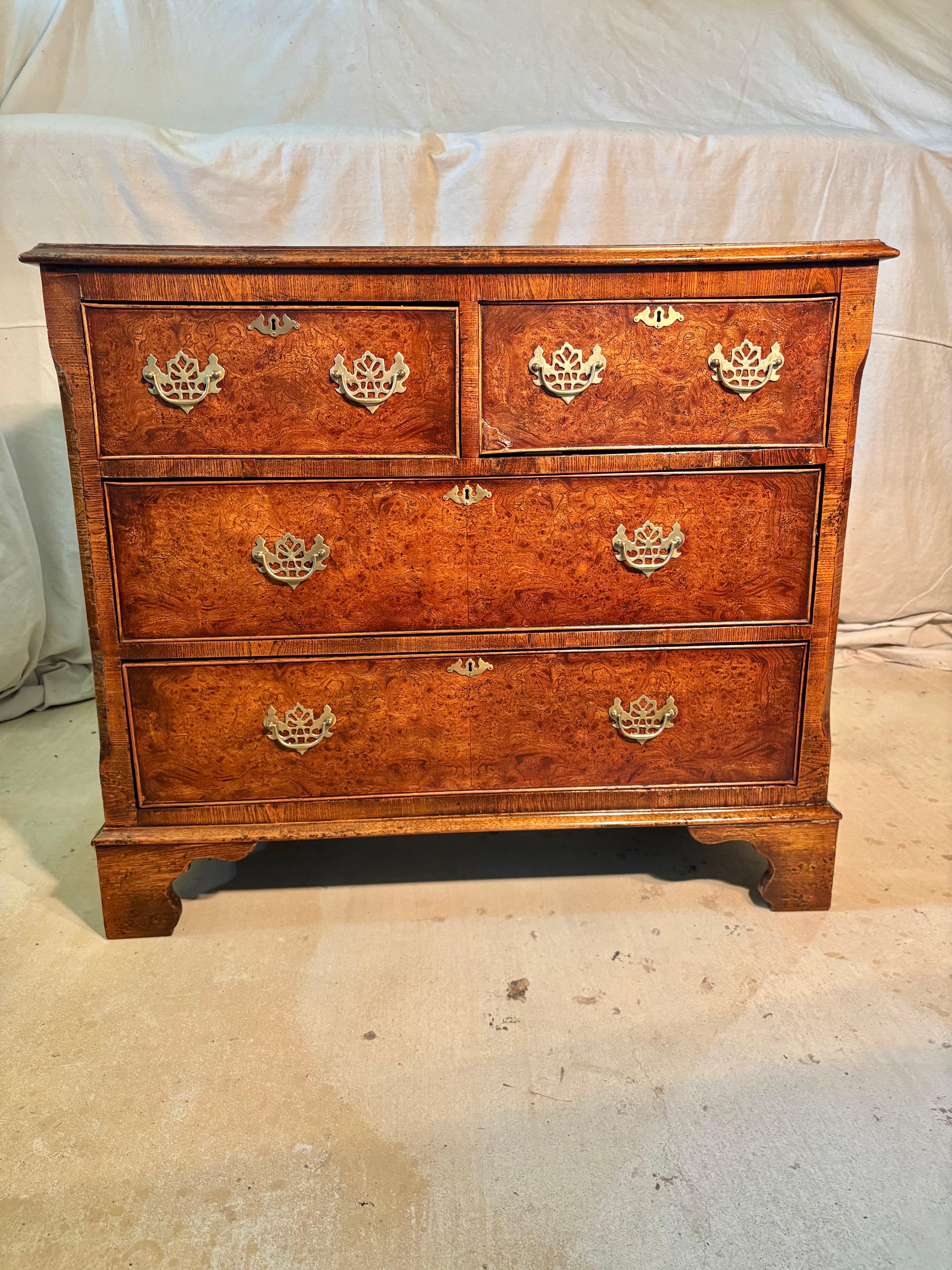 This Late 19th Century English George II Style Chest of Drawers was handcrafted from walnut and burl walnut veneer in the late 1800's. The piece features a banded top resting above four dovetailed drawers, two smaller upper and two larger lower.