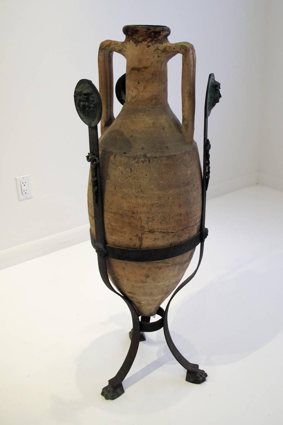 Large Roman Amphora resting on a neoclassical iron tripod stand with patinated bronze Medusa medallions and lion paws feet. The Amphora dates back to the Roman Empire era and is set in a grand tour stand dating back to the late eighteen or early