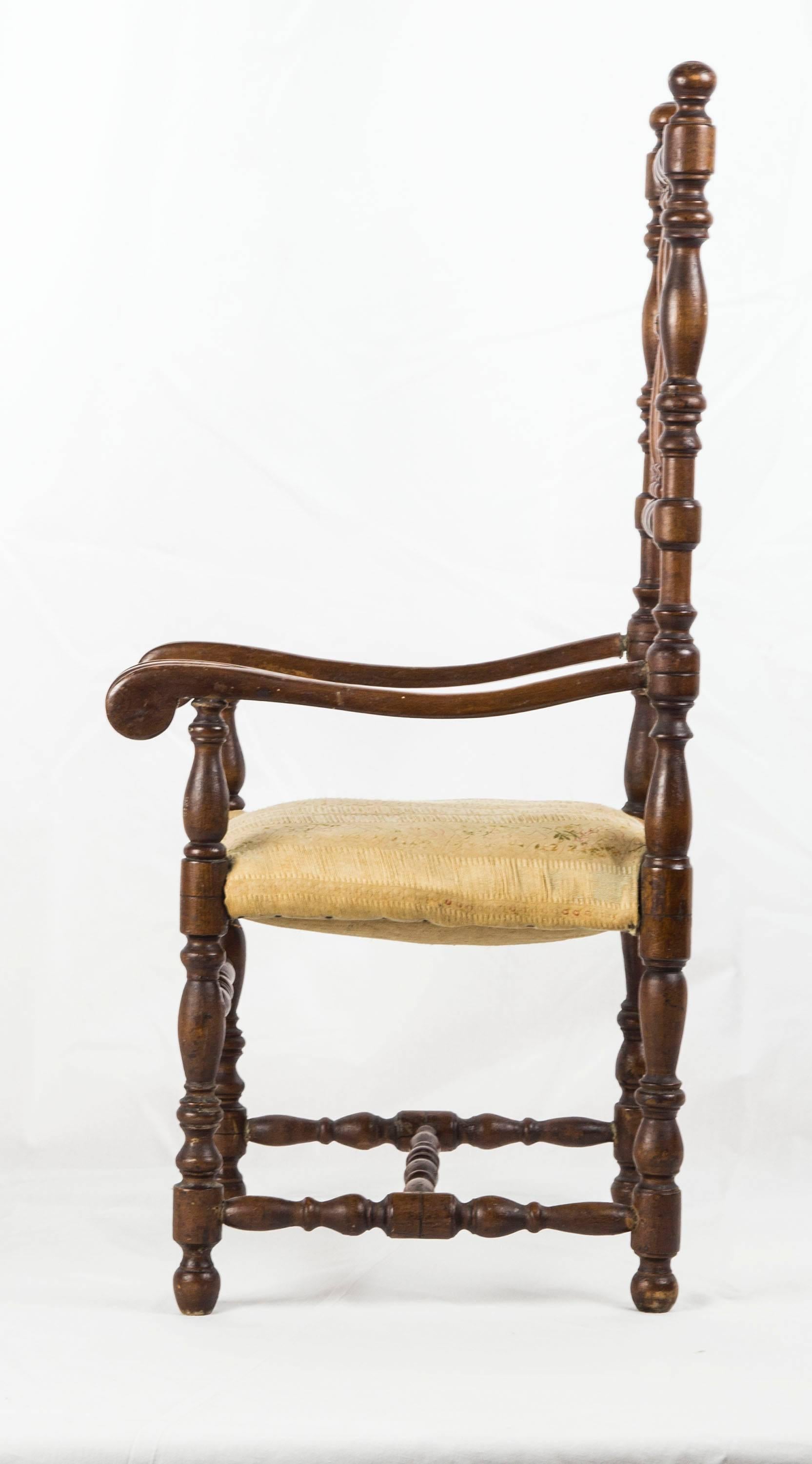 French Louis XIII style walnut open armchair with baluster turned spindle back over carved arms and raised on turned legs with H-stretcher; the seat is stuffed with horsehair and upholstered in yellow ribbon silk.