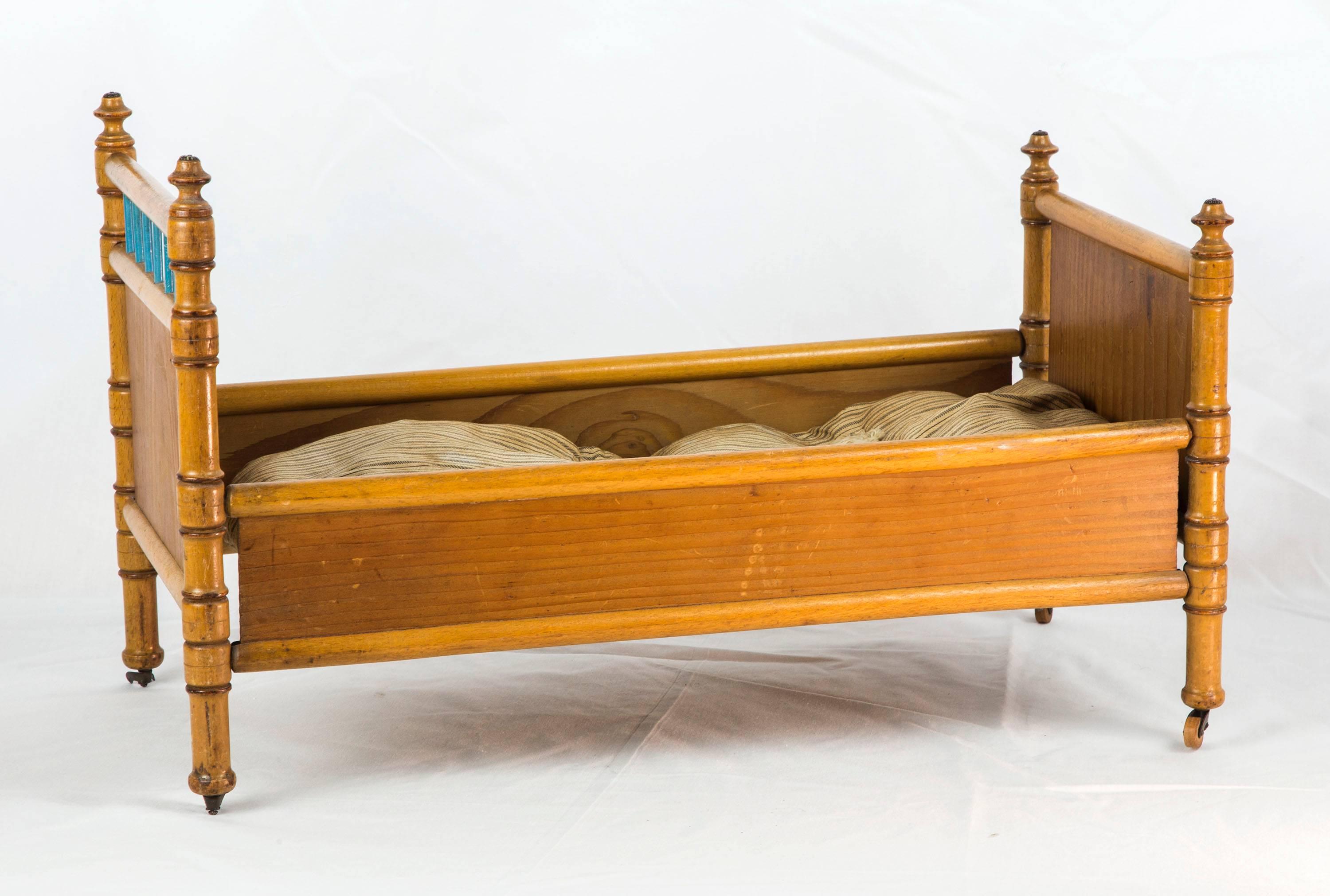 French doll's bed in pine green enameled spindle trimmed headboard and plain foot-board joined by maple bordered sides with maple turned legs with star-shaped finials on iron and wood casters (two casters missing). The spindle-joined frame base