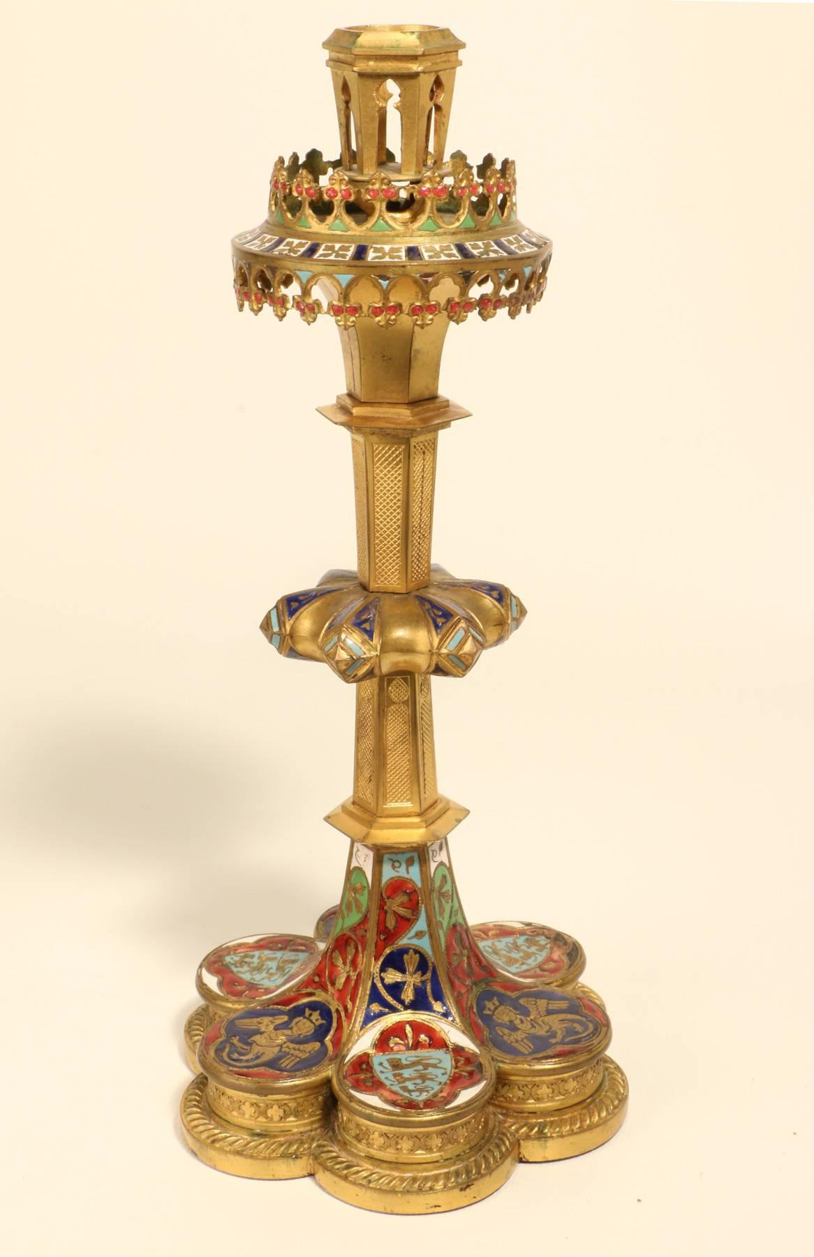 A rare pair of antique English Neo-Medieval gilt bronze and enameled candlesticks, each raised on a gadrooned lobed hexafoil base, enameled with alternating roundels depicting a shield with three leopards of graduated size, and a metamorphic figure