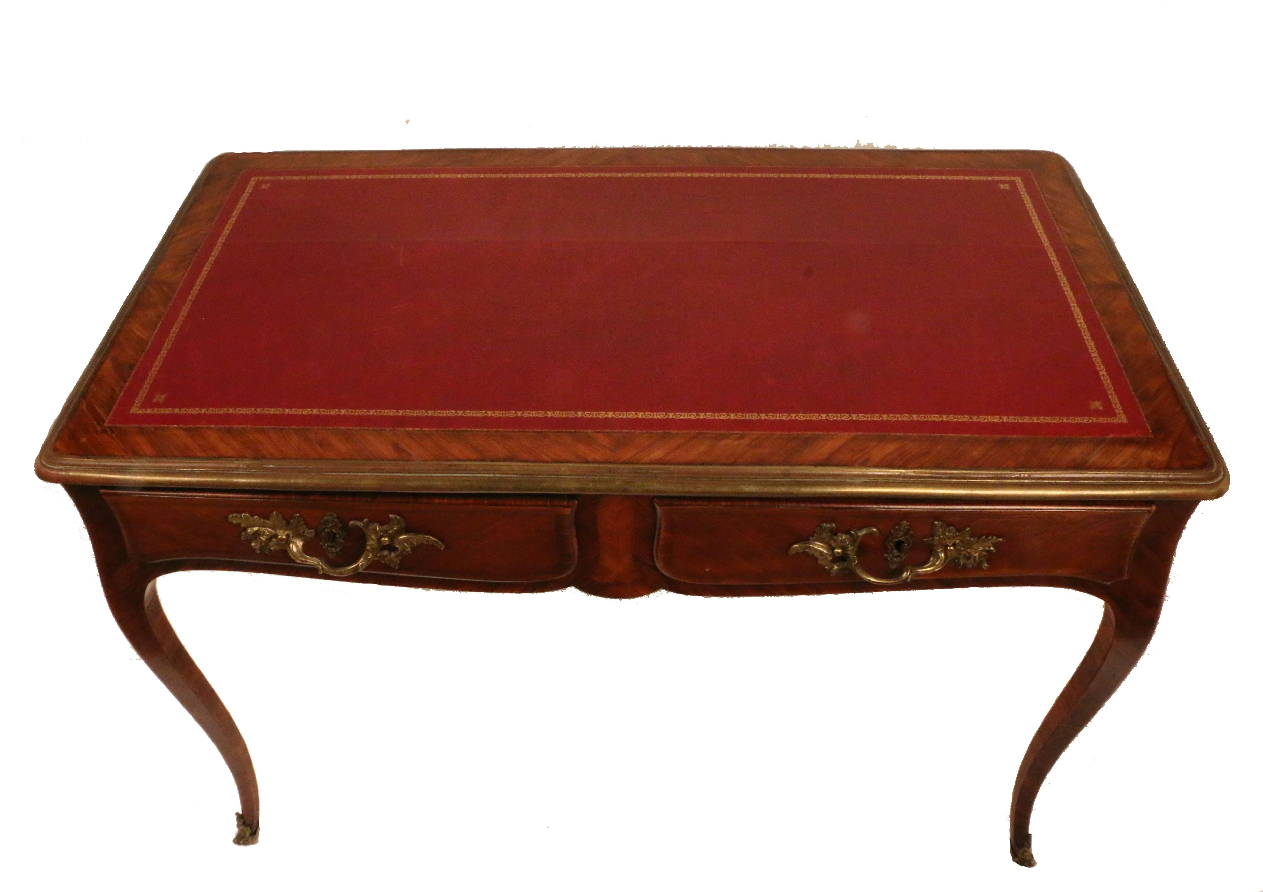 Elegantly understated, this bureau plat is a very useful size. Veneered in violet wood with two frieze drawers, it retains its original handles and sabots and has a tooled red leather writing surface with a conforming bronze surround. The front is