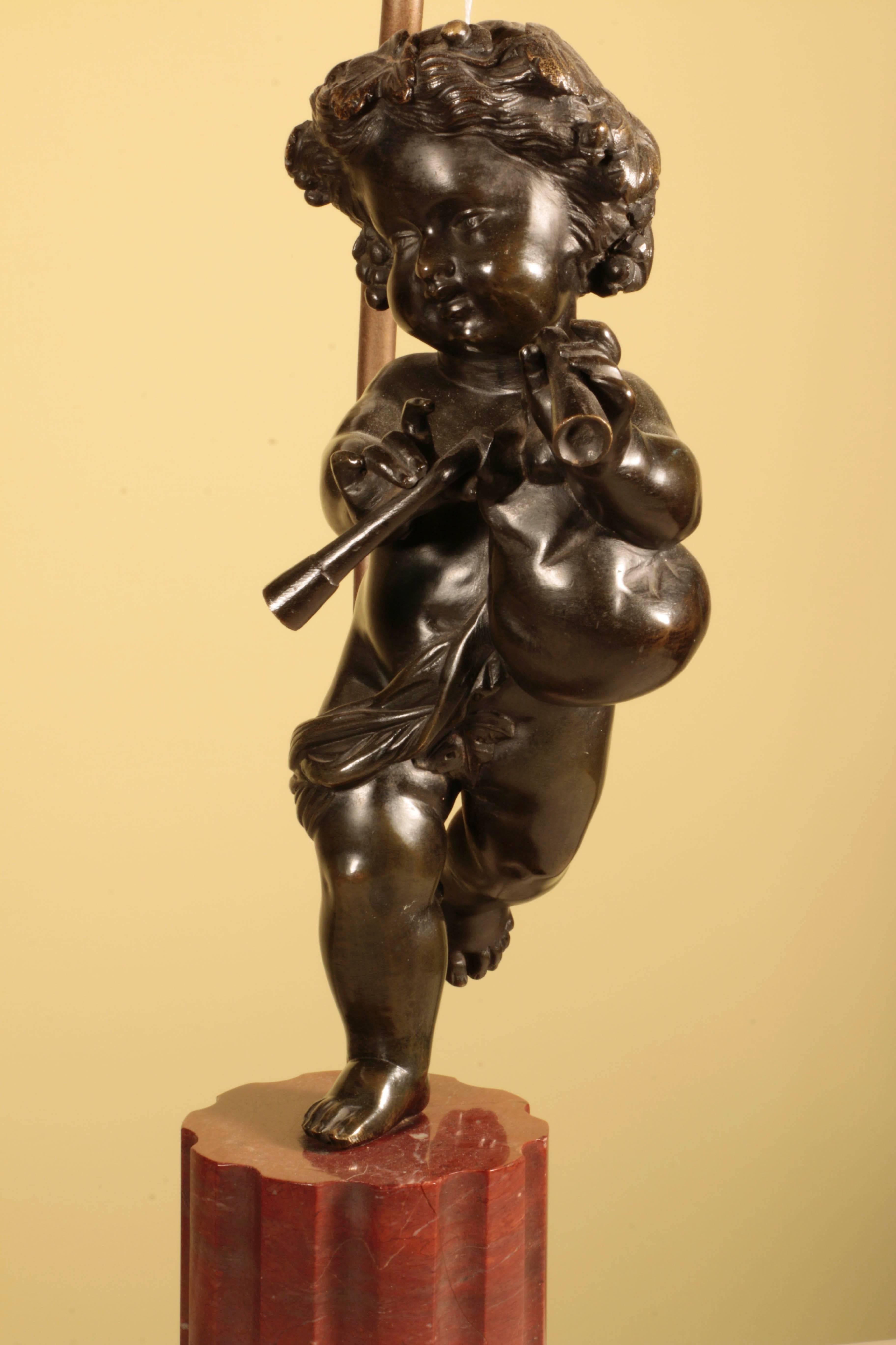 Paire de putti en bronze patiné à la manière de Clodion, 
l'un tenant une cornemuse, l'autre un oiseau ; chacun surmonté d'un 
colonne cannelée en marbre rouge sur socle octogonal, montée en tant que 
lampes avec abat-jour personnalisés.