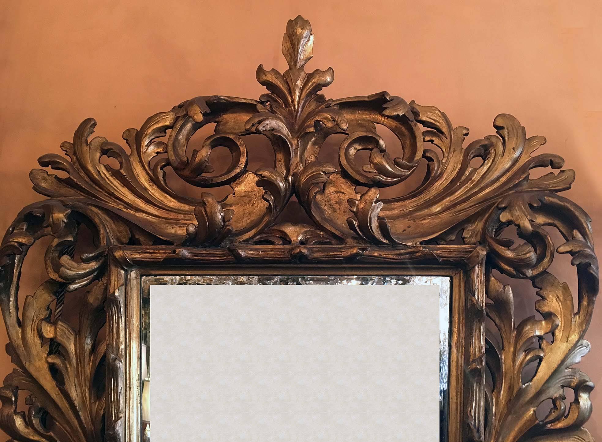 This later beveled mirror plate is of tapering rectangular shape and is enclosed by a large frame vigourously carved with scrolling acanthus.
The mirror plate is relatively small and the carved frame quite large. The carving is exuberant. It has a