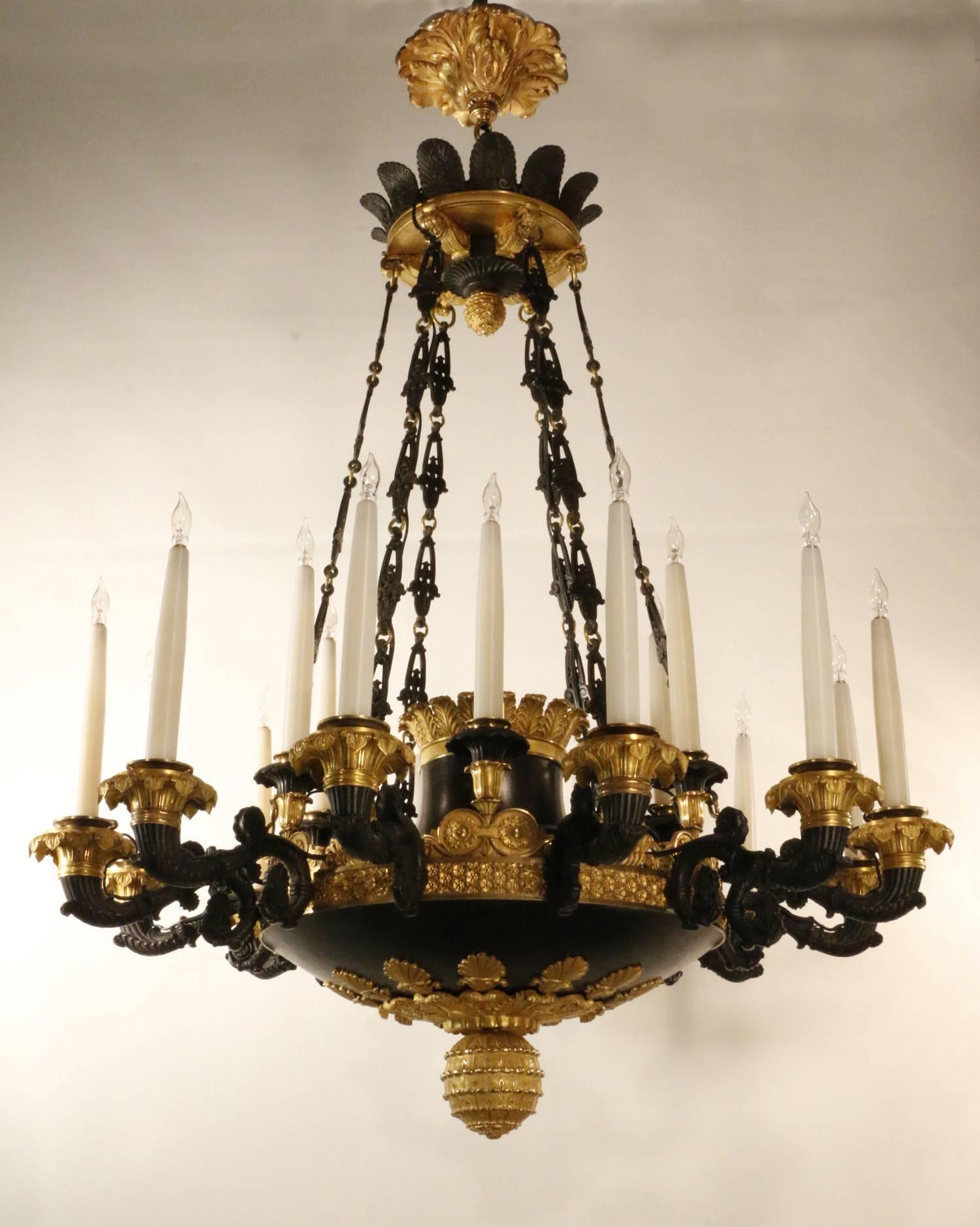 Spectacular French early 19th century bronze and ormolu chandelier, the 12 scrolling arms  molded with leaves and interspersed with six additional lights, the bronze body  partially gilded  and with gilt bobeches, stylized acanthus, garlands and