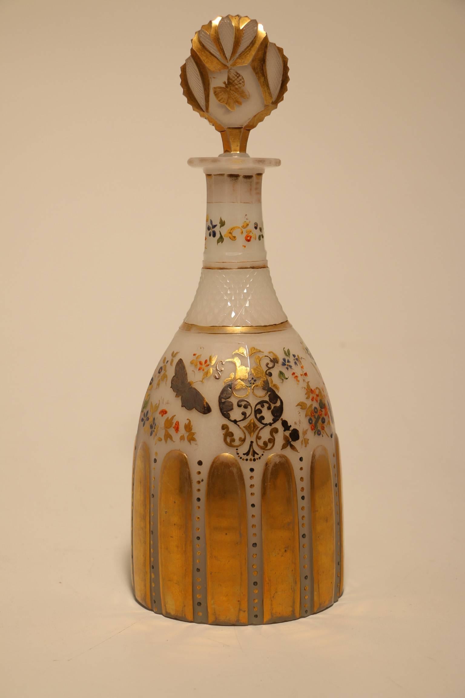 A hand-painted and cut opaline glass decanter with stopper. The neck cut with a band of raised diamonds, the  faceted body with raised and gilt vertical bands,  freely painted and gilt with wild flowers, trophies and a butterfly. The stopper is