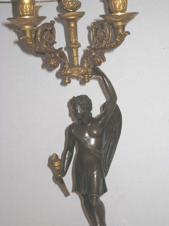 Pair of patinated and gilt bronze candelabra,  one depicting winged Diana, her upstretched arm holding a crown supporting a four arm gilt candelabra, the other modelled  as  winged Apollo  holding a torch. Each  moumnted on a decorative gilt bronze