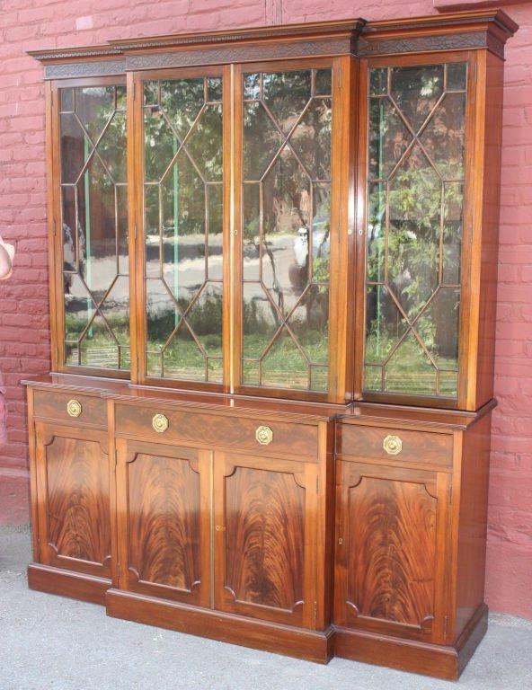 George III style mahogany breakfront three bay bookcase cabinet, the ogee dentillated over blind fretwork cornice with four astragal glazed doors over one long and two short drawers atop four matched flame mahogany doors. Brass tag inside door,