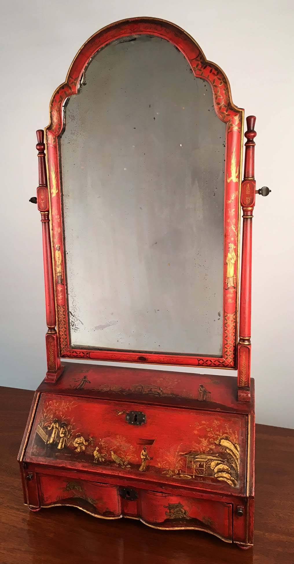 A George I red japanned and gilt toilet mirror, the period plate in double arched and ovalo frame, the stand with fall front and fitted interior above a single shaped drawer en arbalete, the whole gilt painted and in shallow relief with chinoiseries