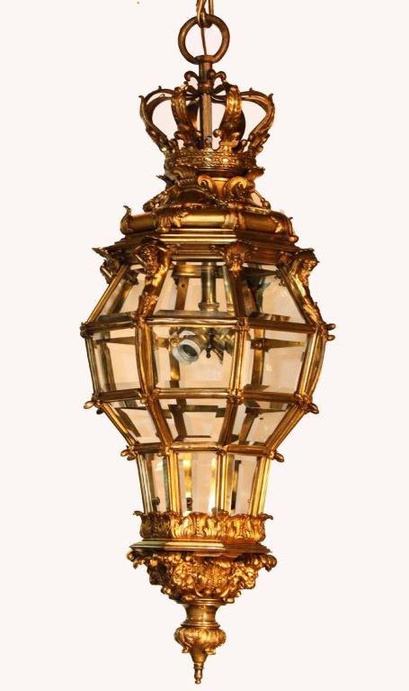 Louis XIV style gilt bronze and beveled glass octagonal four-light Versailles lantern, the corona suspended from heavy links upholds the banded sectional frame enclosing beveled glass panels joined by foliate base enhanced with lion masks, over a