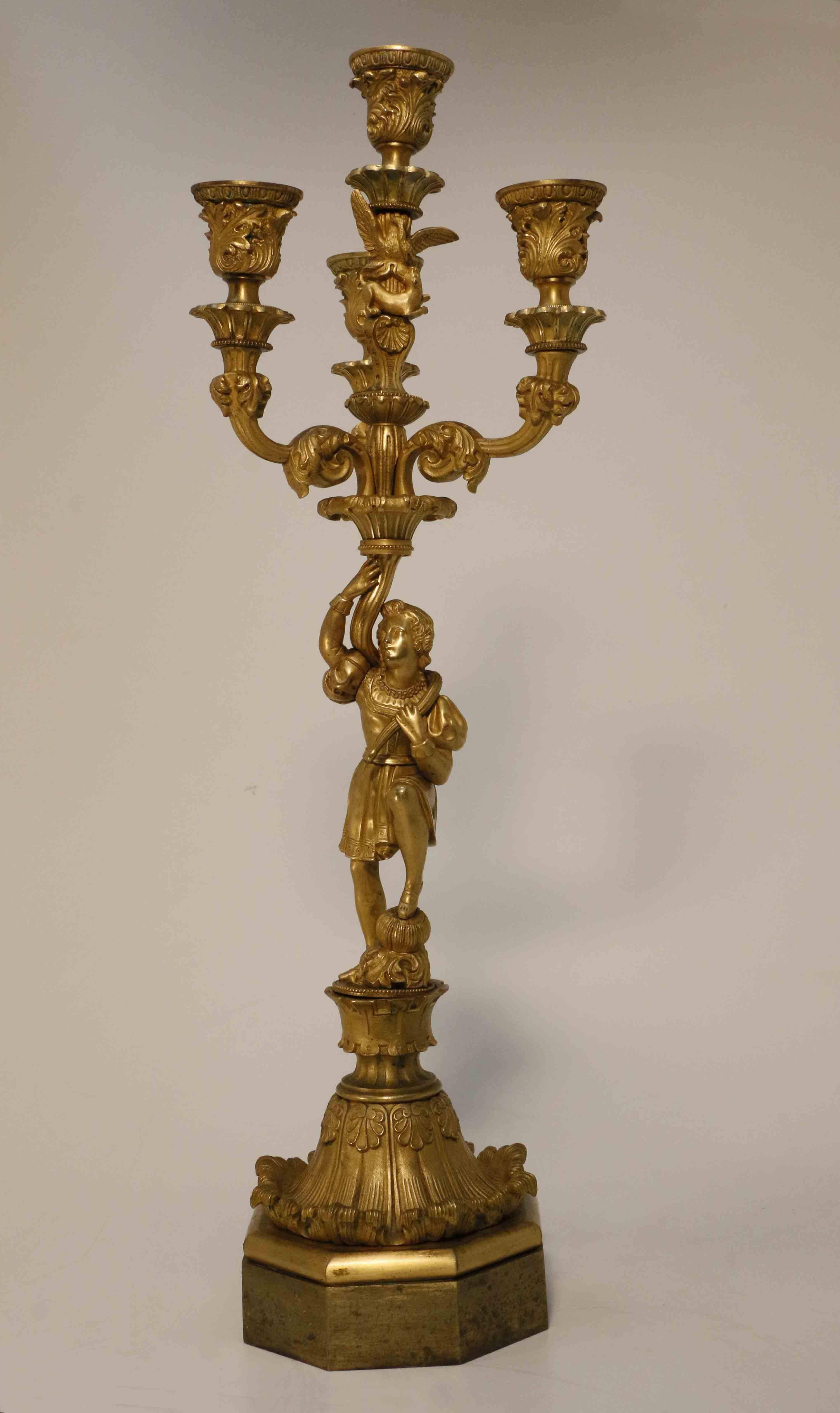 Each well modeled as a youth in Renaissance dress, one foot upon a gourd and supporting a four-light candelabrum, the arms cast with acanthus, the stem cast with a bird and wildcat, the hexagonal base is surmounted by an everted rim of stylized