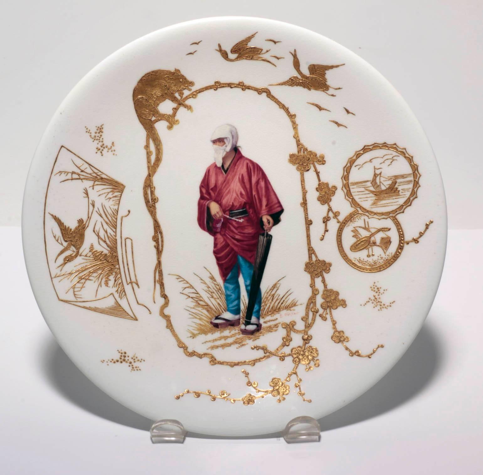 Suite of ten Japonaiserie French porcelain cabinet plates. Each painted in polychrome with a single Japanese figure, at a different pursuit, framed within a raised gilt border depicting a stylised dragon and prunus blossoms on a pale cream ground.