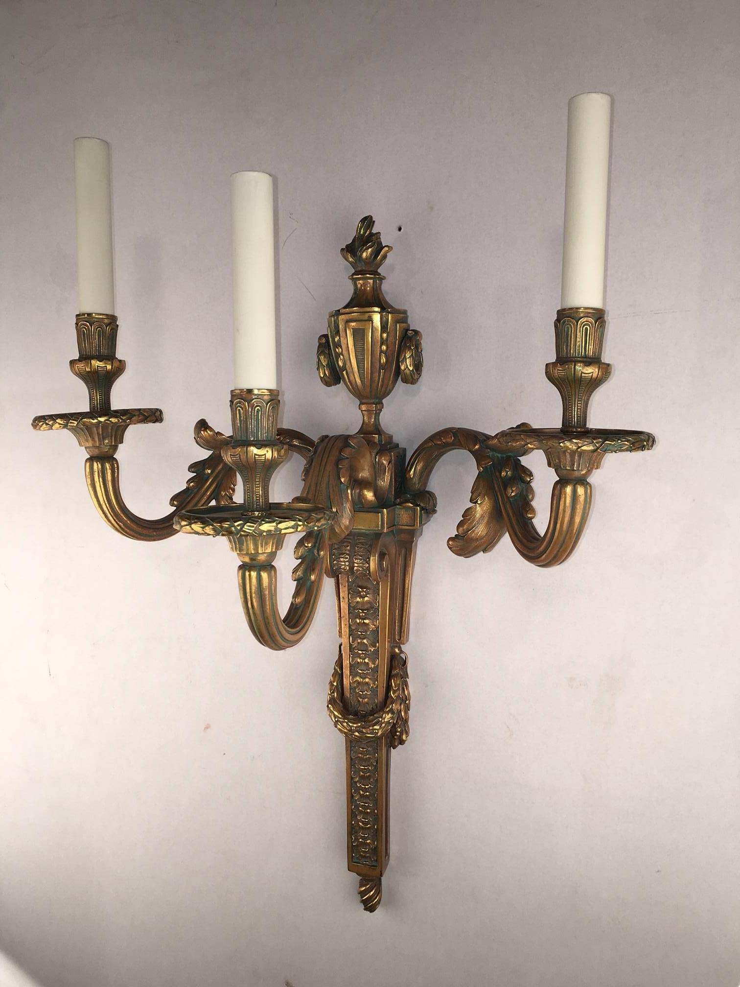 A massive pair of Louis XVI style three light bronze wall sconces, each arm modeled with scrolling acanthus, the back plate with vase-shaped flame finial and of tapering garlanded form cast with leaves and berries.