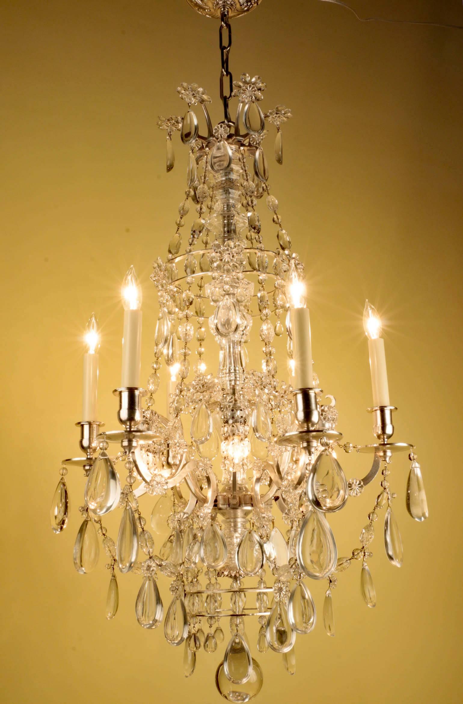 A fine French silvered bronze 12 light chandelier, This elegant chandelier is surmounted by a crown of floral rosettes and half-pear pendent drops; swags of cut drops cascade to a lower tier and thence to silvered arms which are again connected by