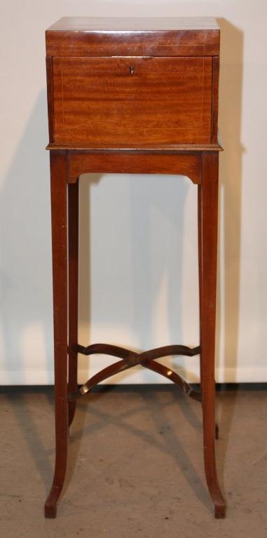 Edwardian mahogany parfumeuse on stand with tapered legs joined by arched cross stretchers; the hinged lid lifts to reveal beveled mirror over slide above two drawers, behind the slide are four compartments fitted with stoppered bottles; to the side