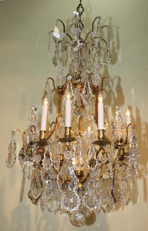  This fixture has many excellent qualities. The cage frame is gilt, the central stem is clad in crystal,, the arms and candle sockets are slender and elegant. There are nine arms and one illuminating the central spire. It is beautifully hung  with