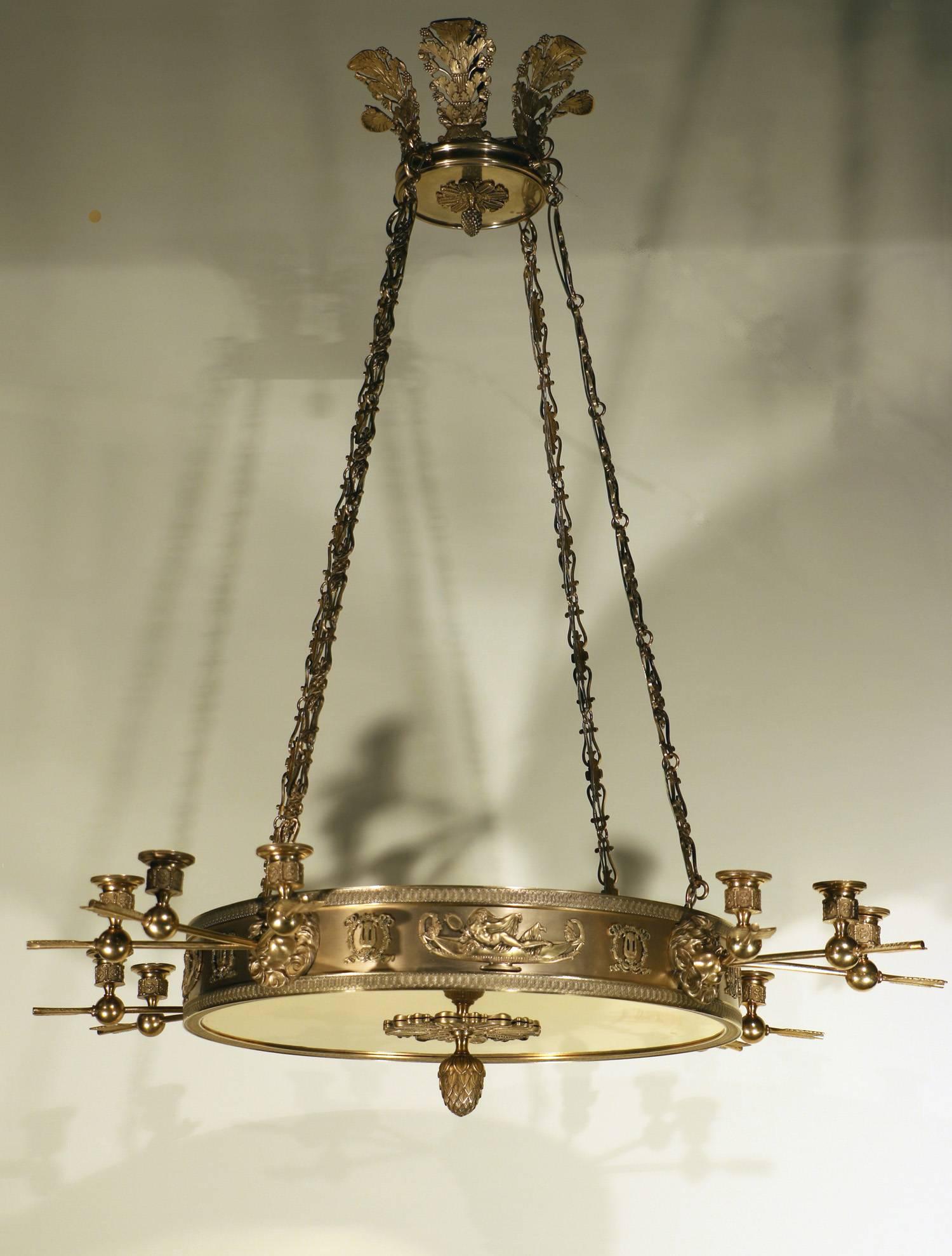 French Empire chandelier in two-tone gilt bronze. With eight interior light sockets and 12 candle cups on fleche arms protruding from lions mouths on a decorative band with cartouches of Greek maidens reclining in boats and lyres in wreaths. All