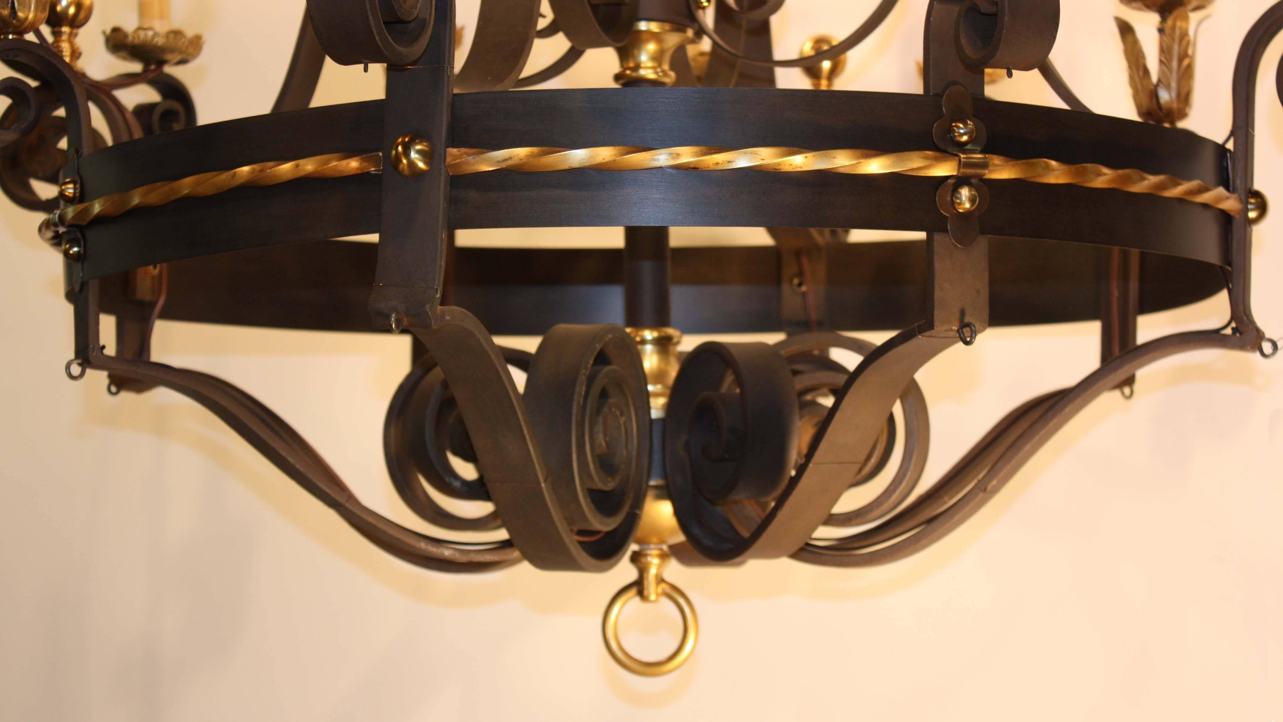 A massive antique ballroom chandelier; the frame in scrolling wrought iron, the upper tier with eight lights, the lower with 12, enriched with patinated brass drip pans, finials, and decorative banding. This imposing chandelier was removed from an