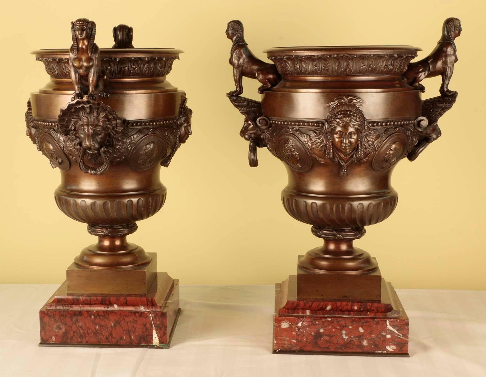 Matching pair of Napoleon III Empire style oiled bronze urns seated on red marble bases. Each urn decorated with facing sphinx resting on lions heads,
with busts of men and women in relief in the central band of the urns.
Pair of Napoleon III bronze