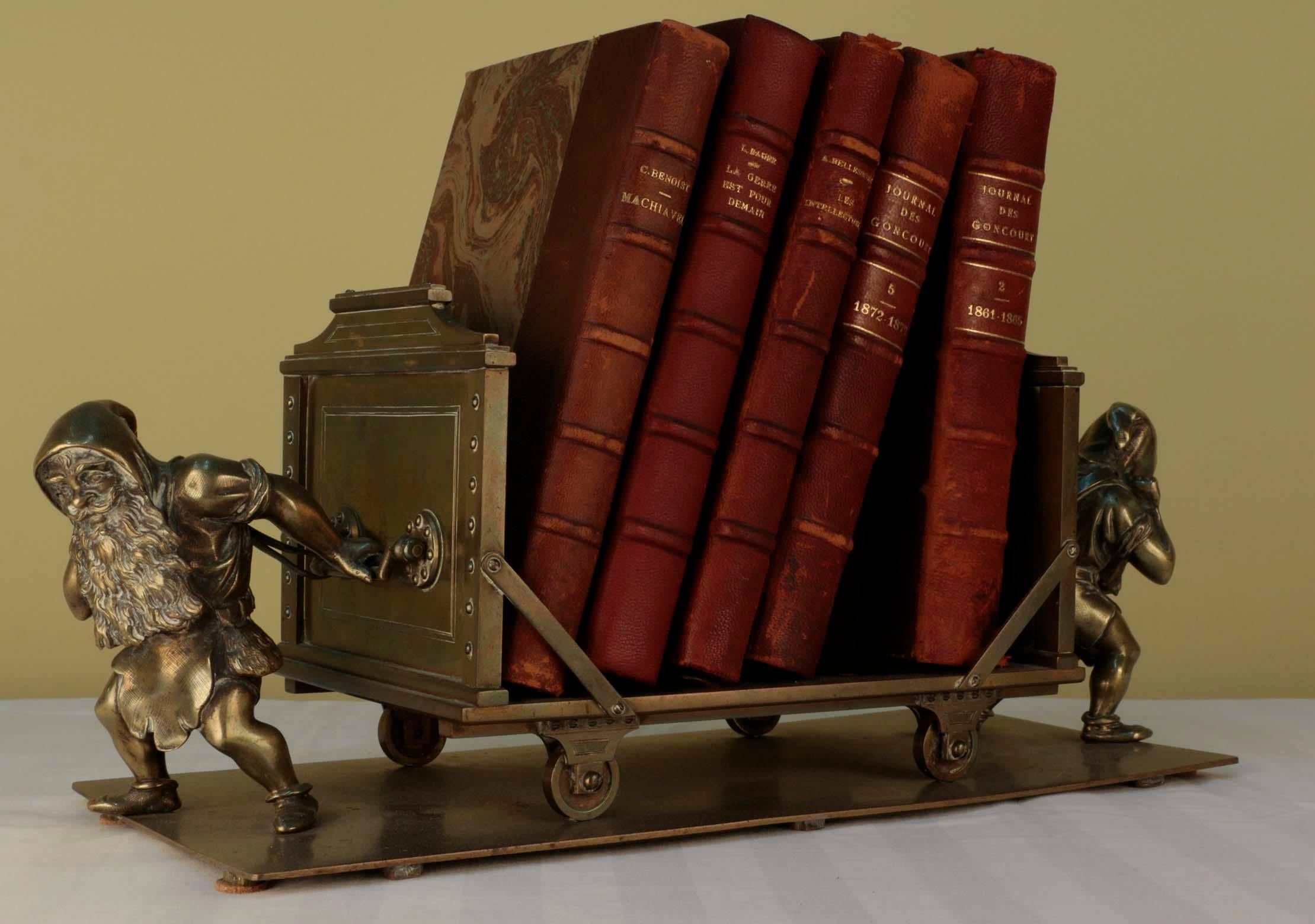 An amusing antique Austrian bronze book stand, well-modeled as a mining cart flanked by dwarfs, each pulling in a different direction.