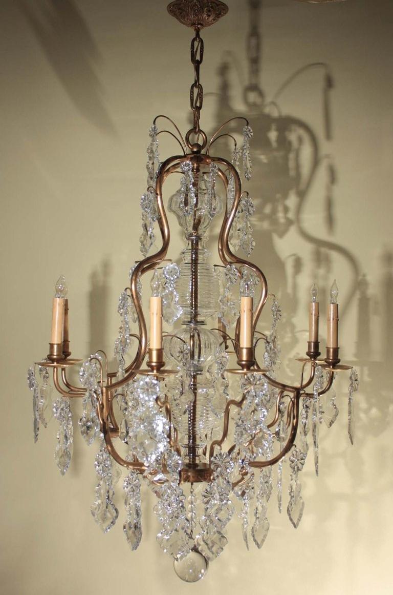 Lampadario a otto luci in stile Luigi XV, la forma  gabbia centrata da un albero di cristallo, pesantemente carico di cristalli pendeloque francesi e terminante con un terminale a sfera. 