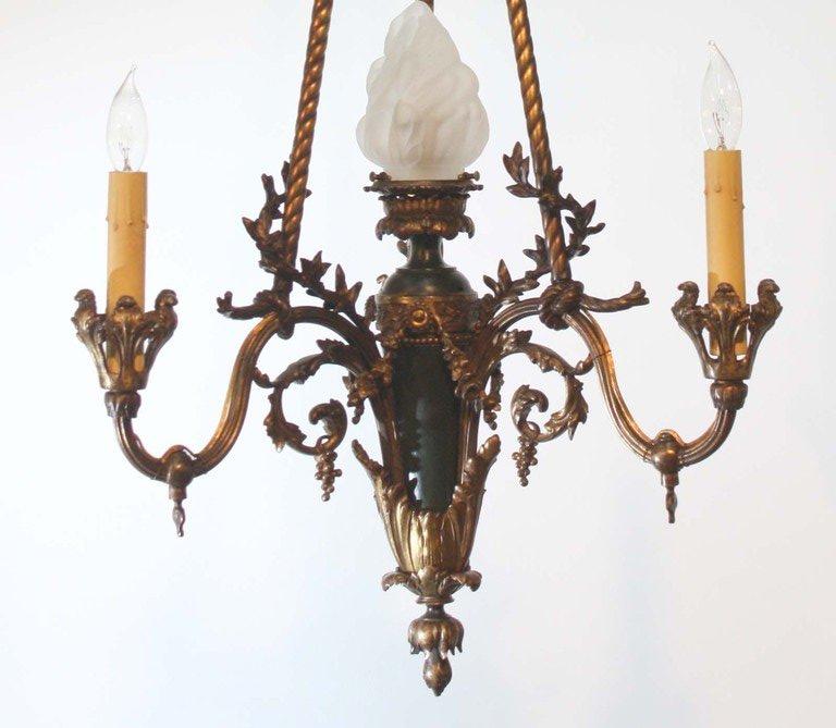  This French patinated and gilt bronze gasolier with central flambeau shade is  suspended from rope twisted rods with ribbon-tied canopy and  three subsiduary candle arms. It has been later adapted for electricity.  This is a fine old chandelier