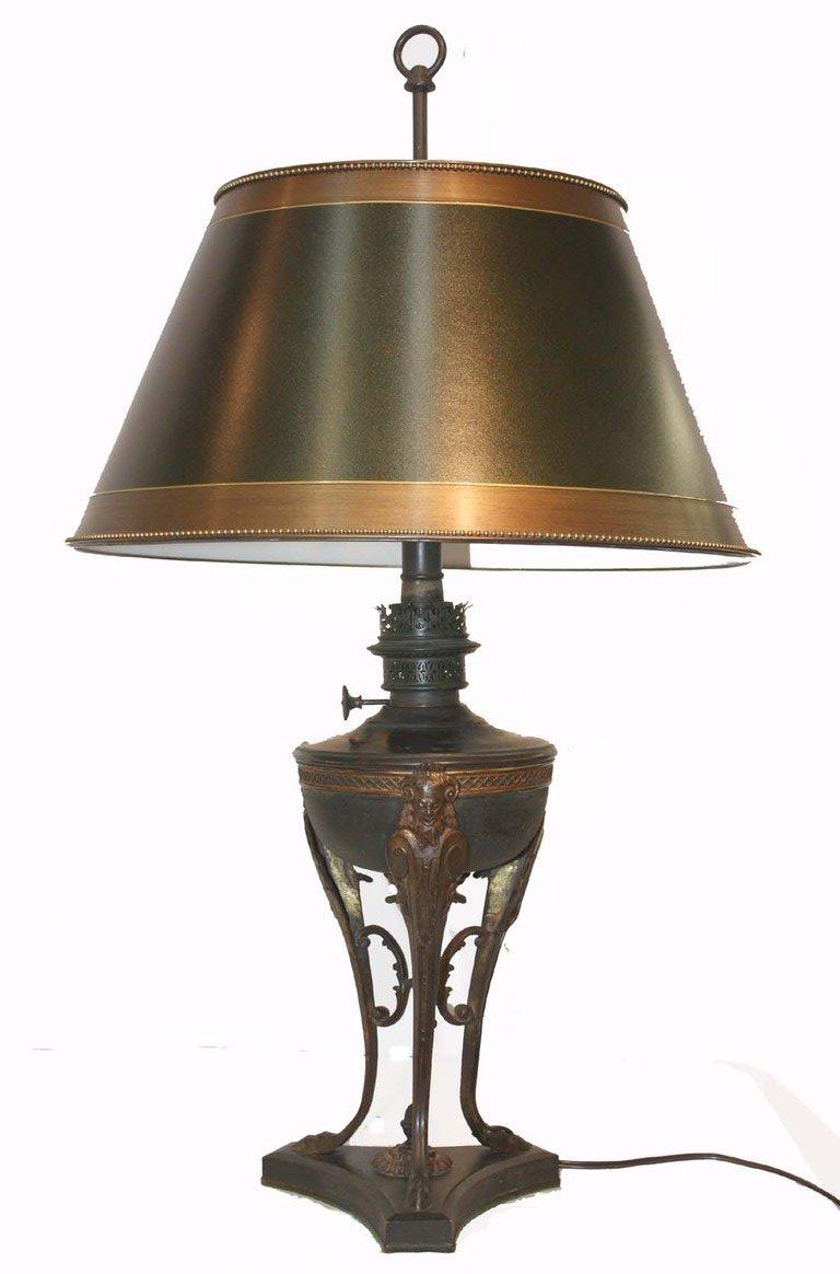 Empire style dark green painted tôle oil reservoir encircled by bronze band raised on cloven hoof tripod feet over incurved base. Later converted to two lite table lamp, with custom height adjustable parchment shade.
This French bronze oil lamp oil