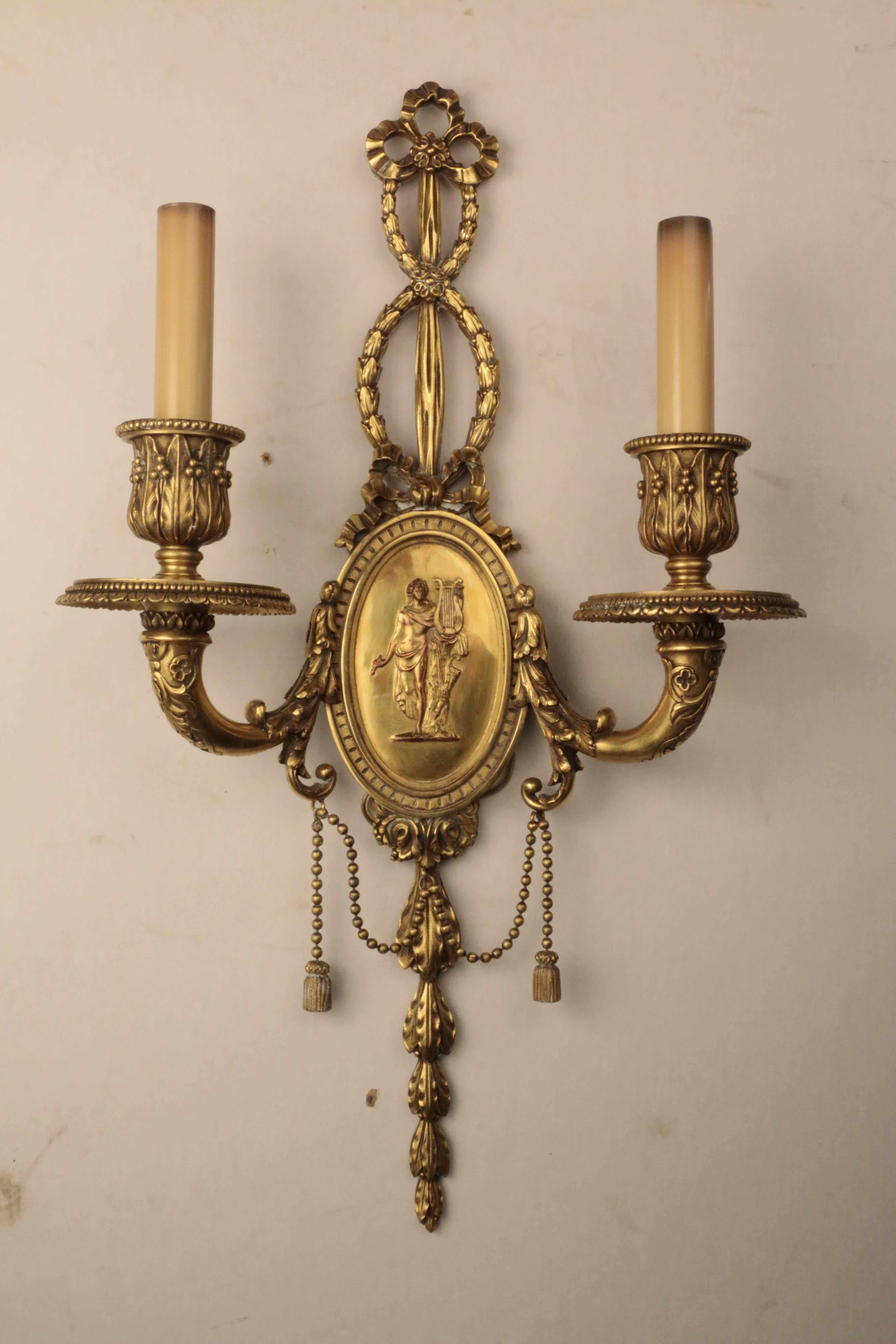 A fine pair of Louis XVI style gilt bronze two-light wall sconces by E F Caldwell of New York, each oval backplate modeled in low relief with an allegorical figure, the muse Calliope. The stem, candle cups and arms are cast with stylized acanthus,