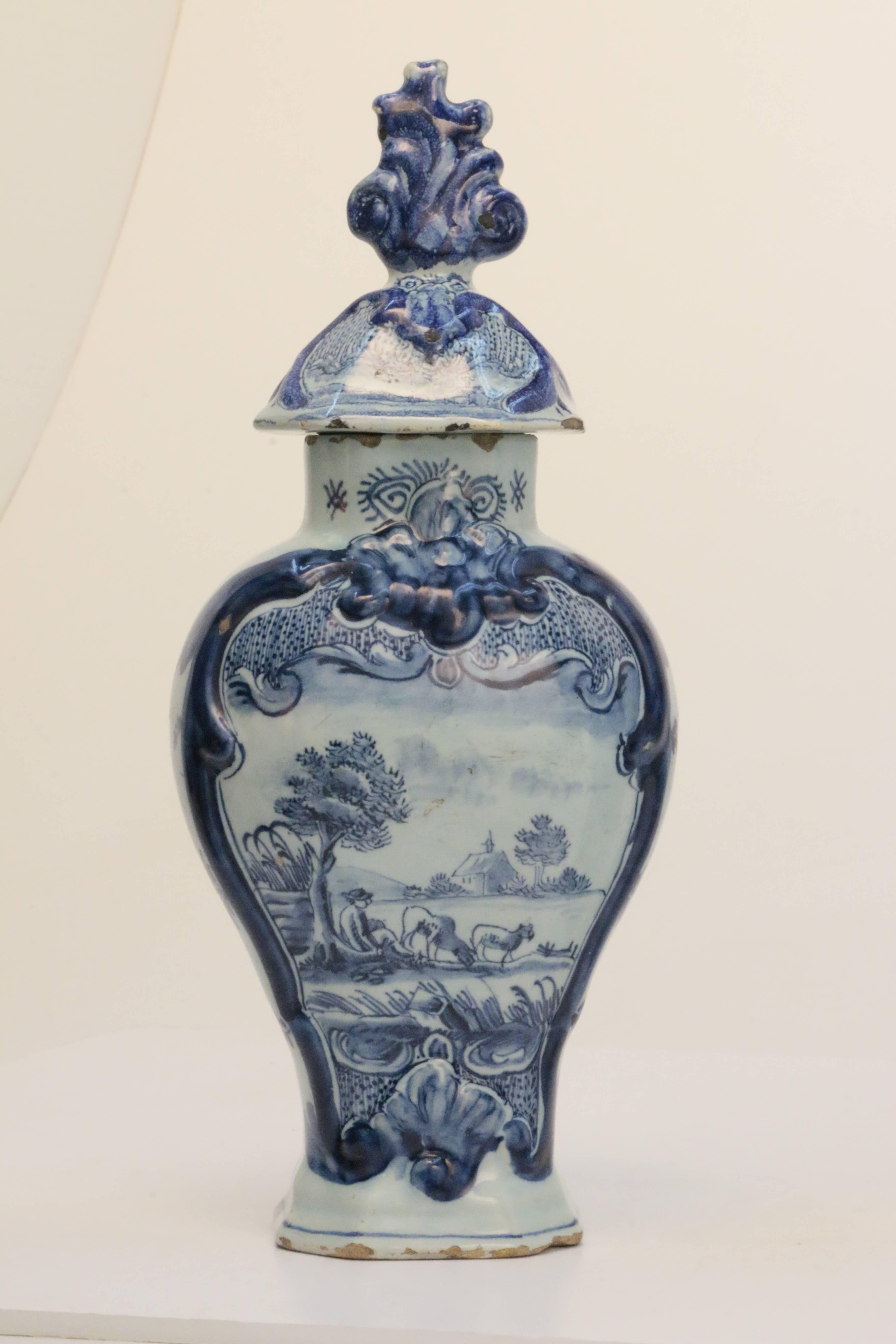 An attractive pair of 18th century Dutch Delft vases, each of molded ovoid paneled outlines, blue painted with a bucolic scene of cows in a pastoral landscape, with original covers with flame finials.

These vases are a Classic example of their
