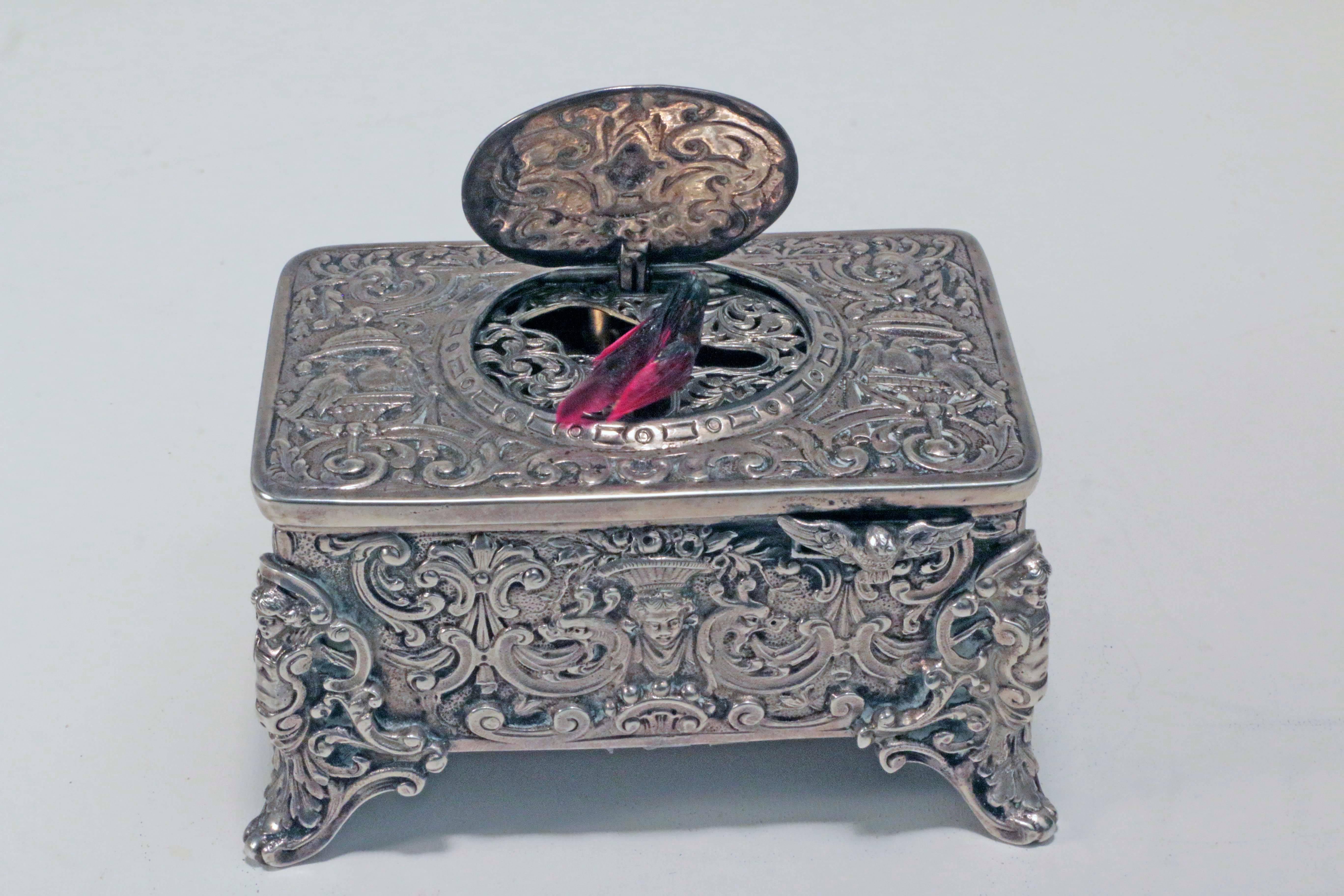 Early 20th century German silver singing bird box by Karl Grisebaum, of typical form. The rectangular box cast with scrolls and caged birds. The central oval cover rising to reveal a tweeting and preening song bird.

Karl Grisebaum's company