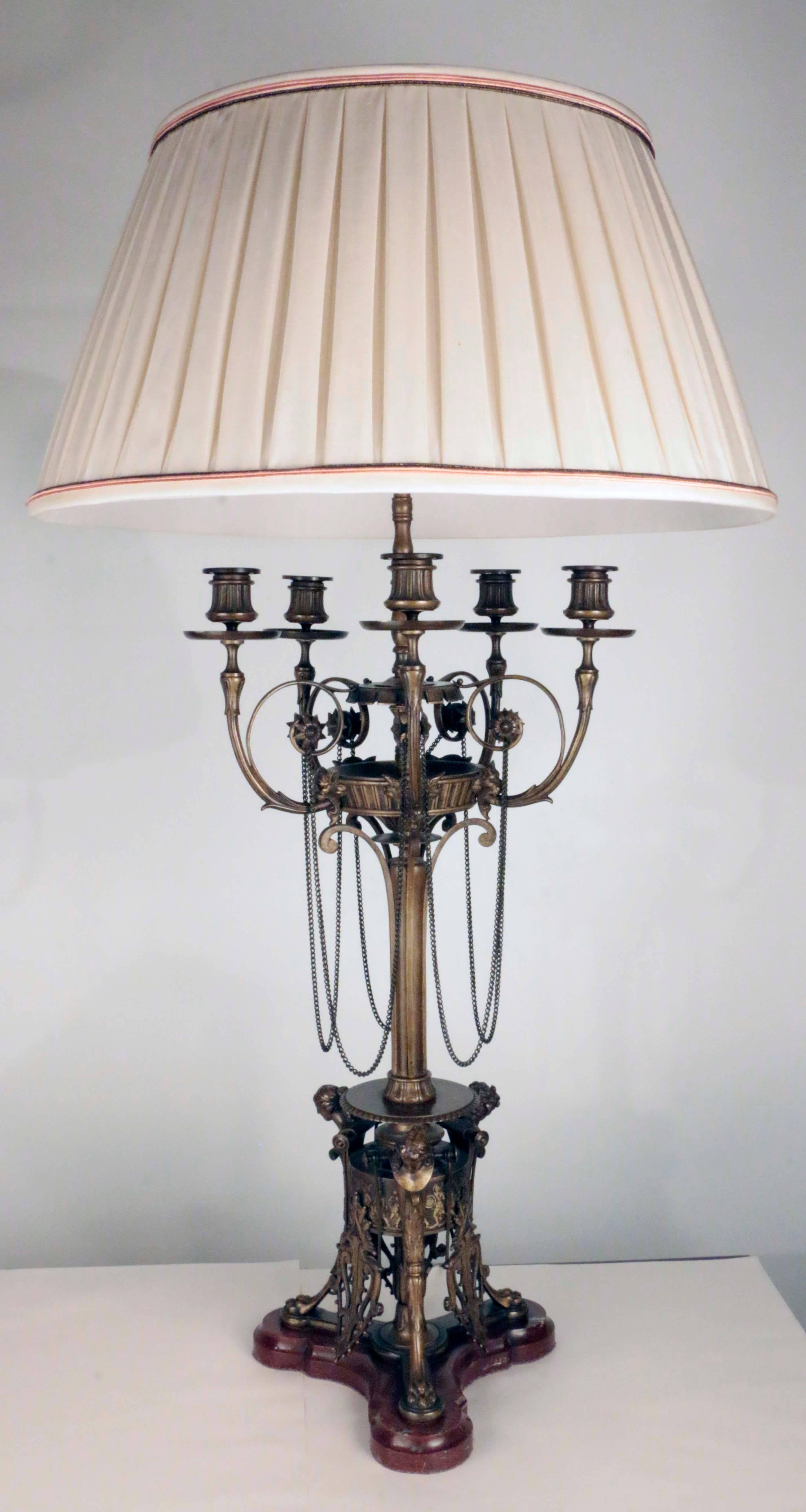 A fine pair of Renaissance Revival  bronze candelabra, now mounted as lamps. Each slender stem supporting five scrolling arms linked by chains, the trefoil platform base modeled with three female heads above paw feet, on a finely beveled and shaped