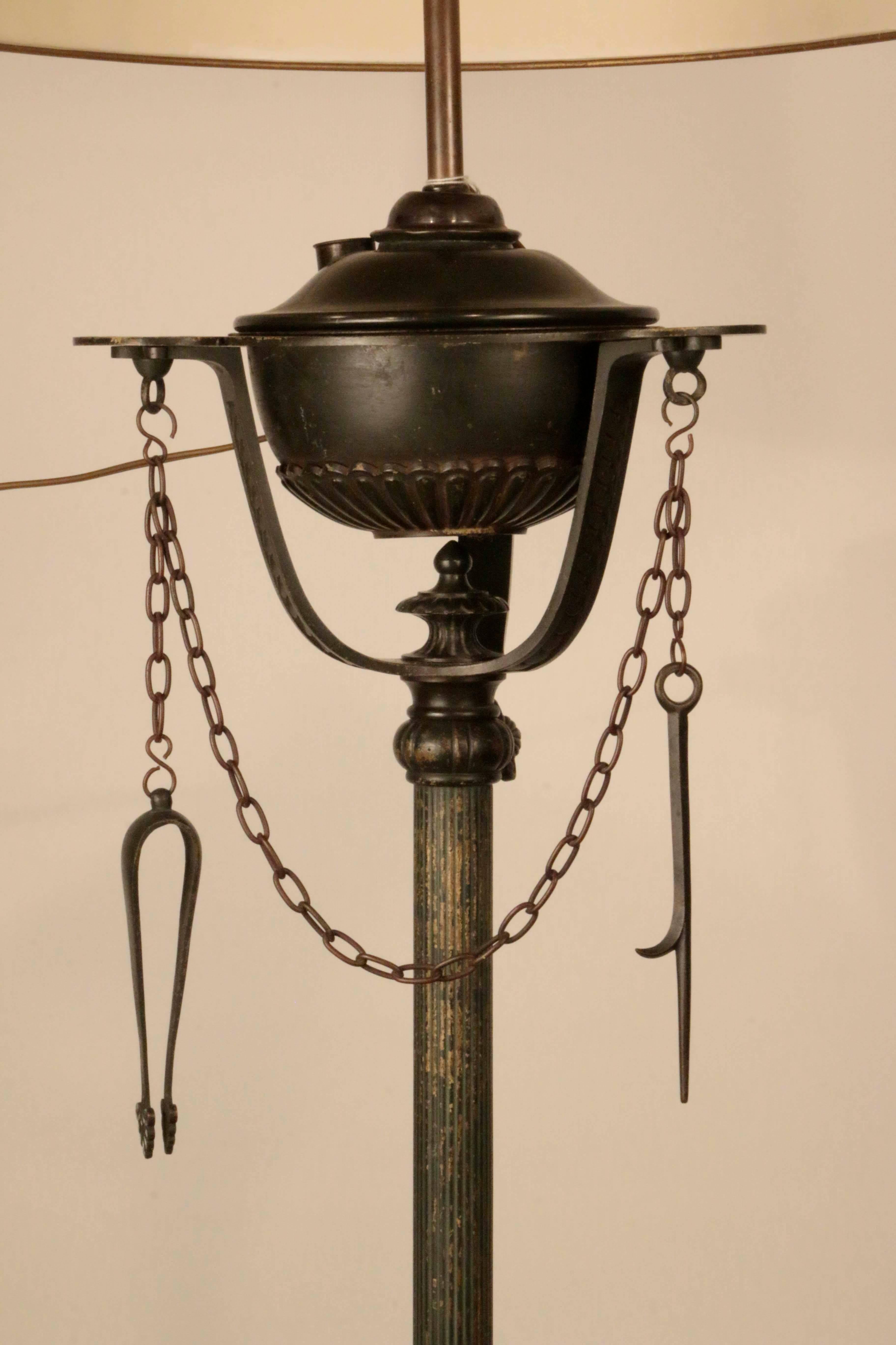 This unusual antique floor lamp revisits in the late 19th century an oil lamp of antiquity. Raised on three cloven hoof feet and with stem encircled by a writhing serpent, the oil reservoir is hung with cleaning tools on chains. While the reservoir