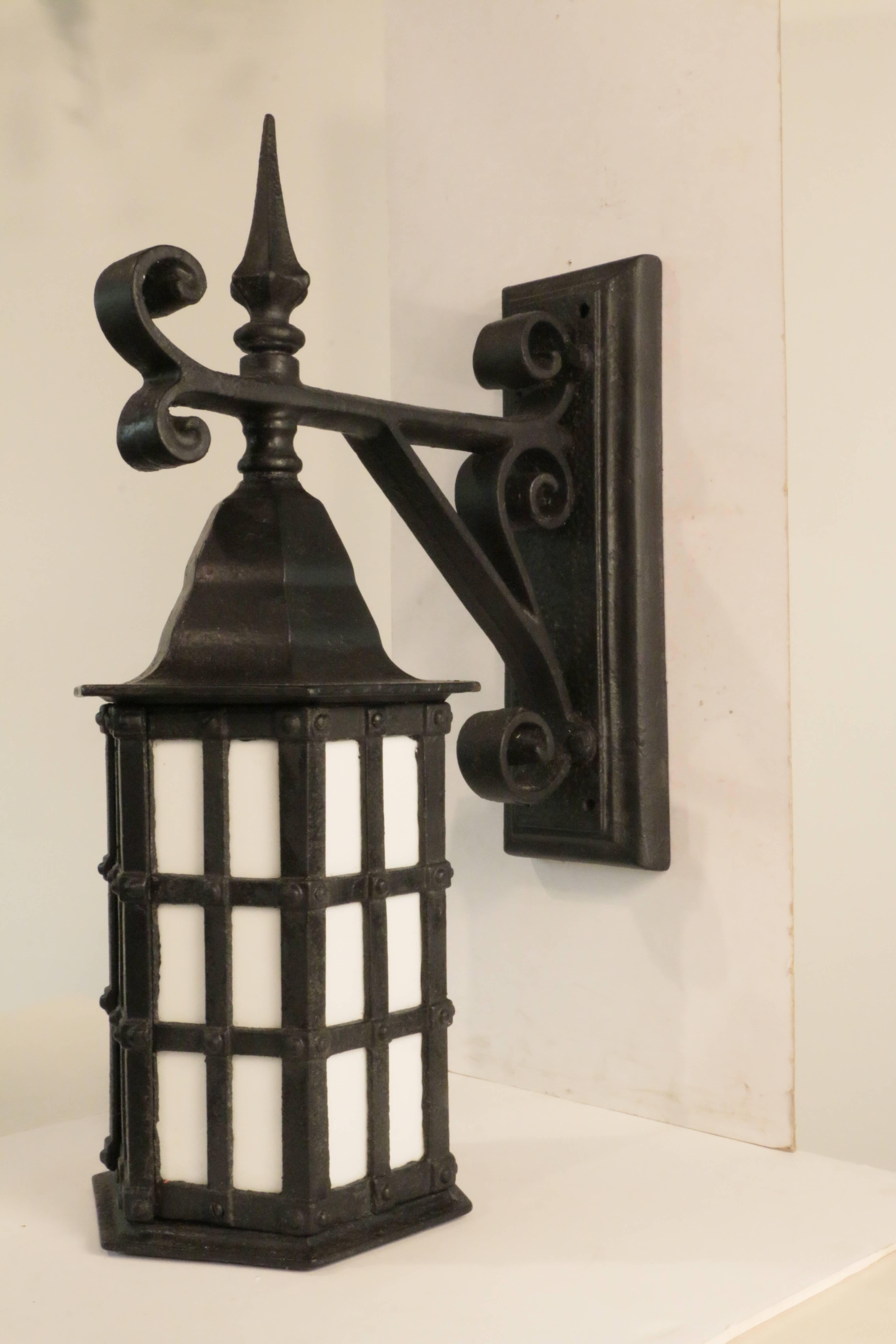 Pair of large cast iron exterior wall sconces,  each a glazed paneled six sided lantern,with conical hood and pointed finial, supported by scrolling braced arm extending from raised rectangular backplate.
American, circa 1900.