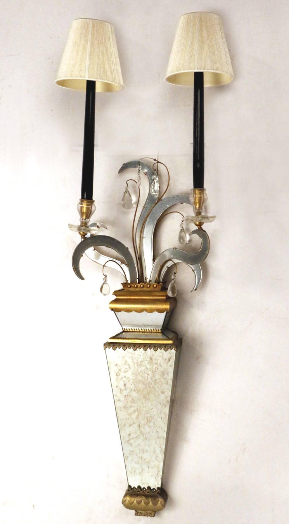 A pair of two-light mirrored wall sconces. This is a rather unusual pair and very stylish, each is of tapering two-tier section, the well- cut drip pans and candle holders supporting slender ebonized wooden candles and pleated shades, supported