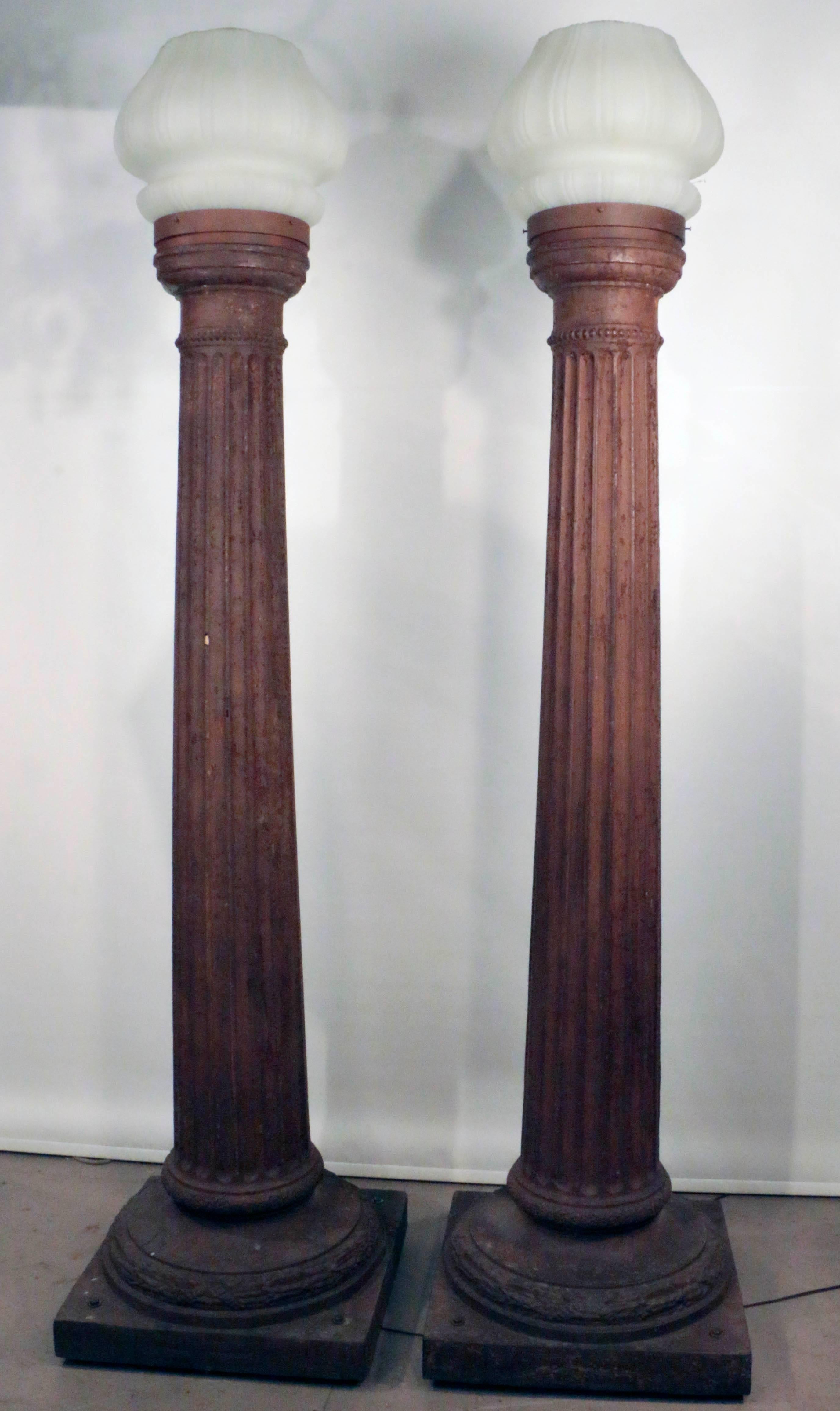 Ein Paar imposanter antiker Gusseisensäulen, die als Straßenlampen montiert sind. Jede dorische Säule ist kanneliert und verjüngt sich von der quadratischen Basis zu einer schlanken Spitze. Jede Säule ist mit einem antiken Milchglasschirm in Form