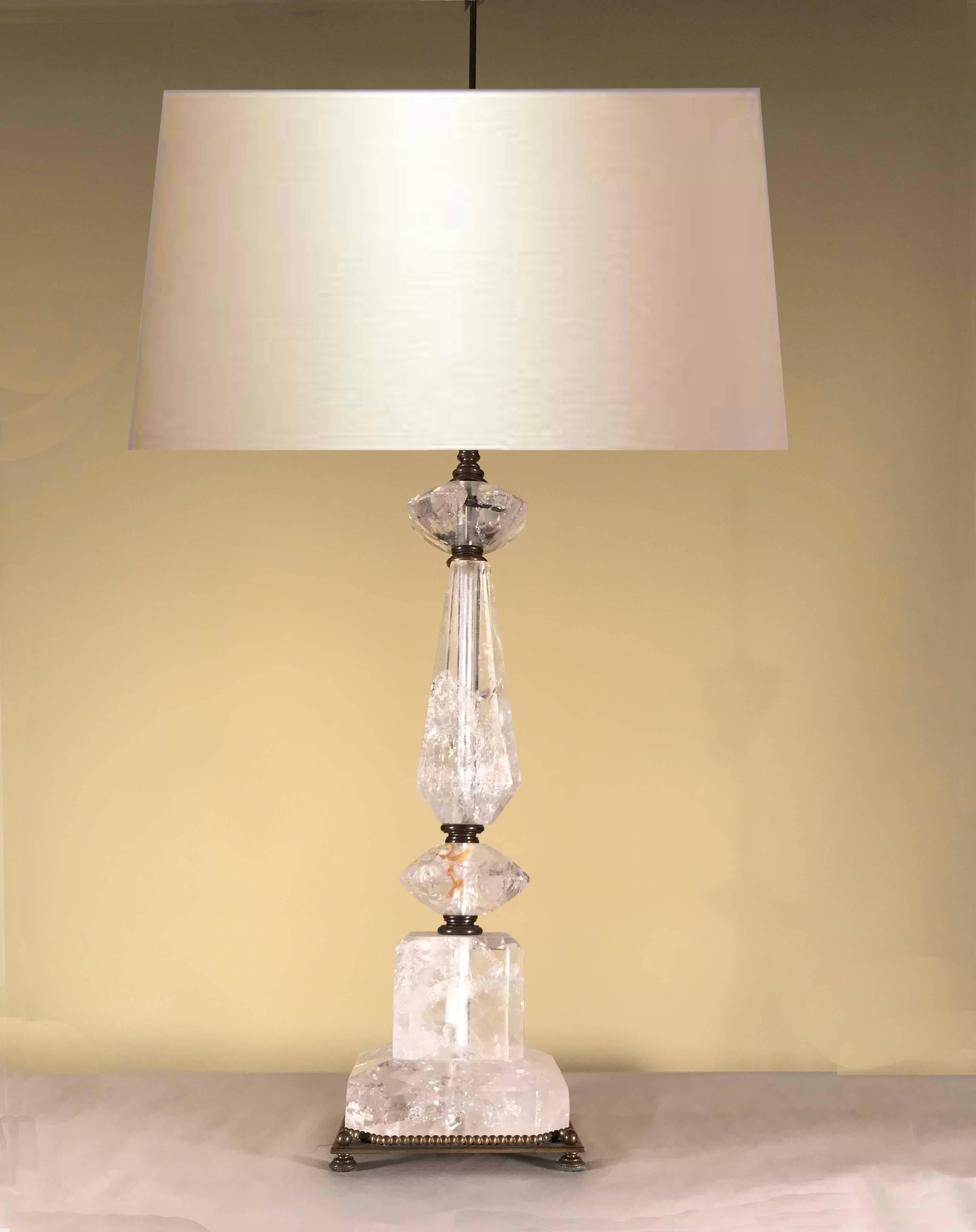 These lamps are modeled with polished shaped geometric rock crystal forms connected by a central rod. The square base is surmounted by a cube surmounted by a tapering faceted stem,  flanked top and bottom by a shaped cut solid trapezoid. The canted