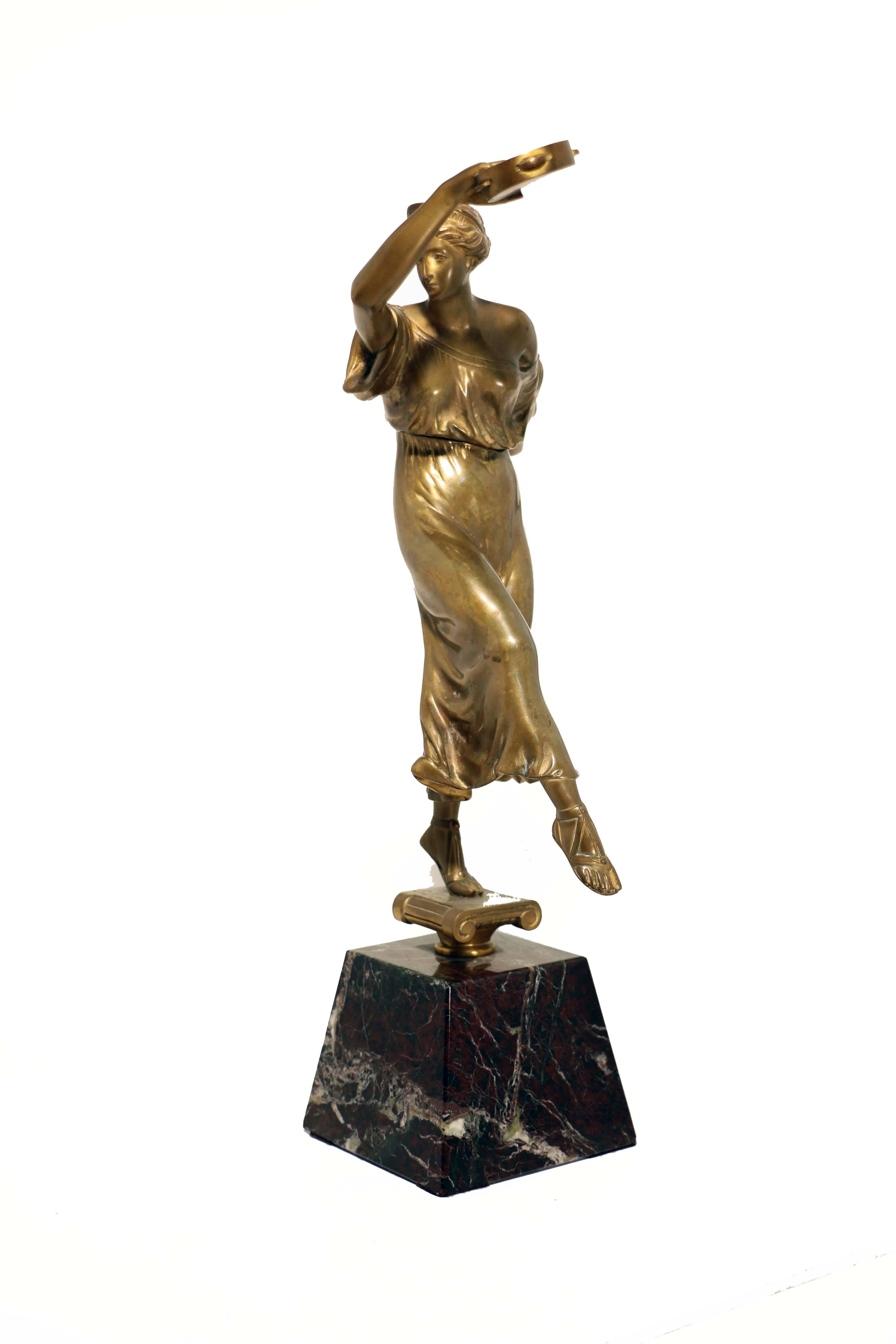 An antique gilt bronze figure of a dancer, after the antique.

The young woman is dressed in a clinging gown and raised on one sandaled foot, her arms hold up two tambourines with which she accompanies her dance. This sensual figure may perhaps be