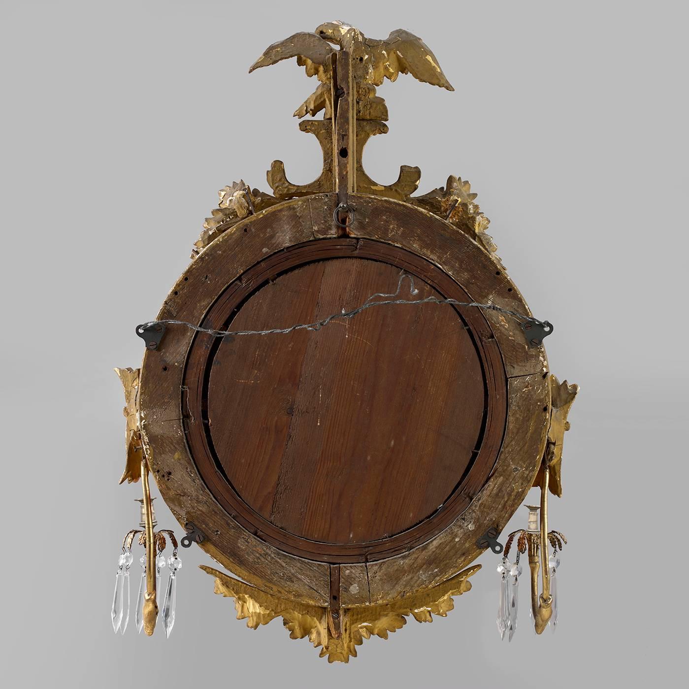 English or American, circa 1800-1820.
Carved giltwood and gesso, looking glass, brass sockets and glass prism.
The convex mirror is surmounted by a carved eagle with outstretched wings perched on a plinth above a circular molded frame with balls