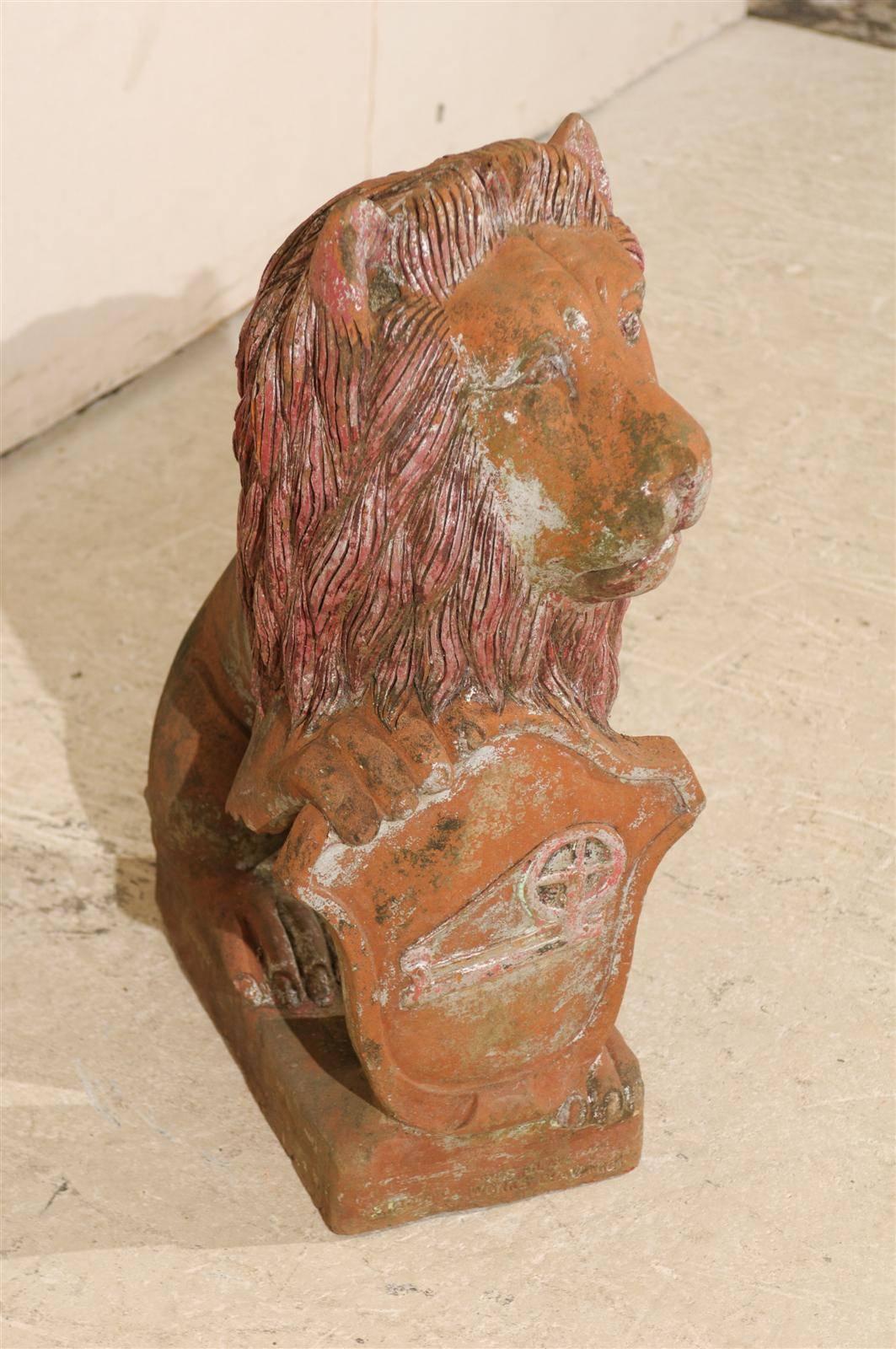 A British colonial terracotta lion floor statue with shield.  This medium sized terracotta lion from India, early 20th century, showcases nice details, such as the texture in the lion's mane, as well as the careful attention applied in the painted