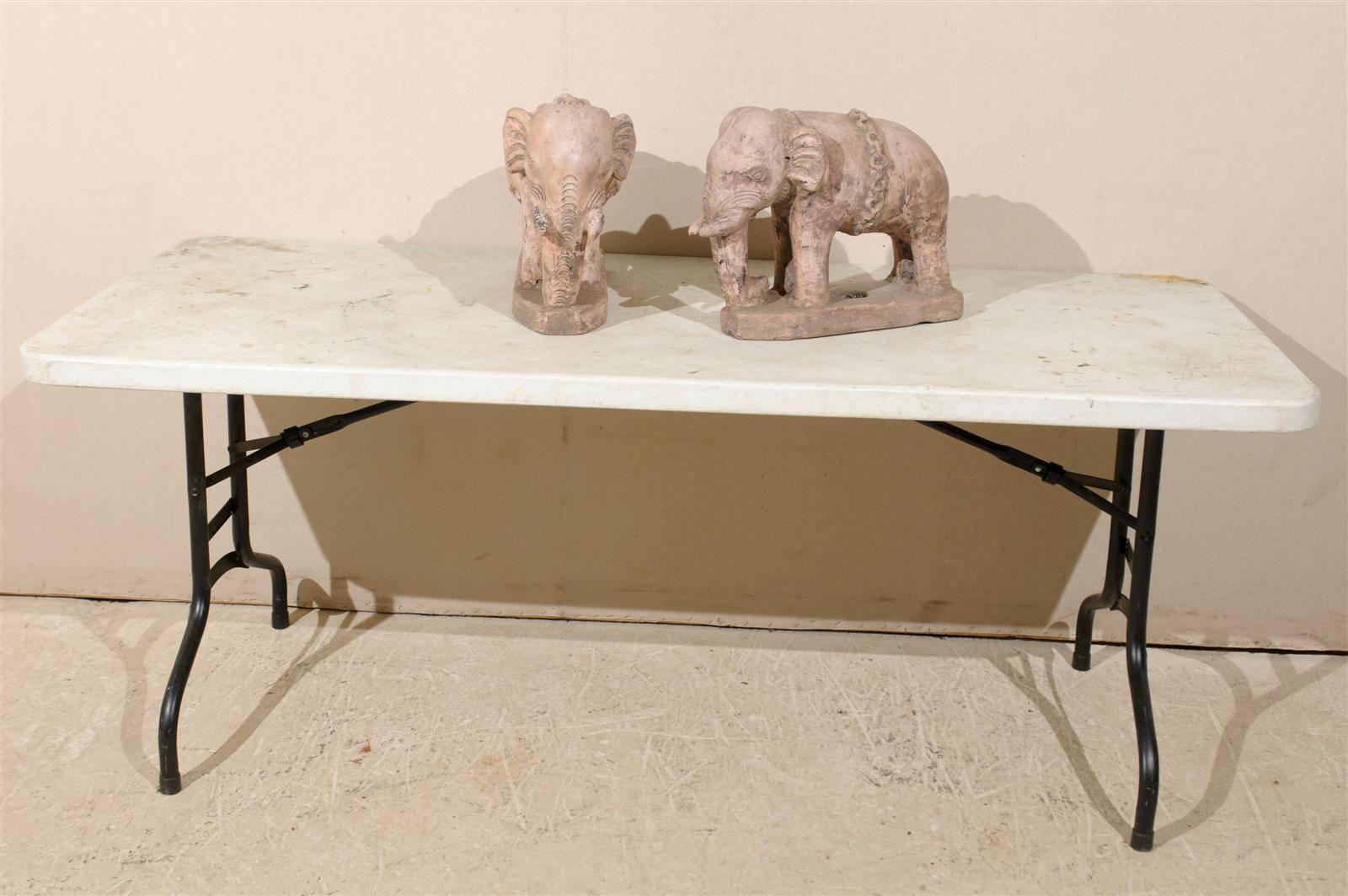 A pair of British colonial terracotta elephants from the early 20th century, India, with nicely rendered details. These eclectic statues have a very subtle, nicely aged, layer of pale pink and beige paint with burnt red and dark rich grey colored