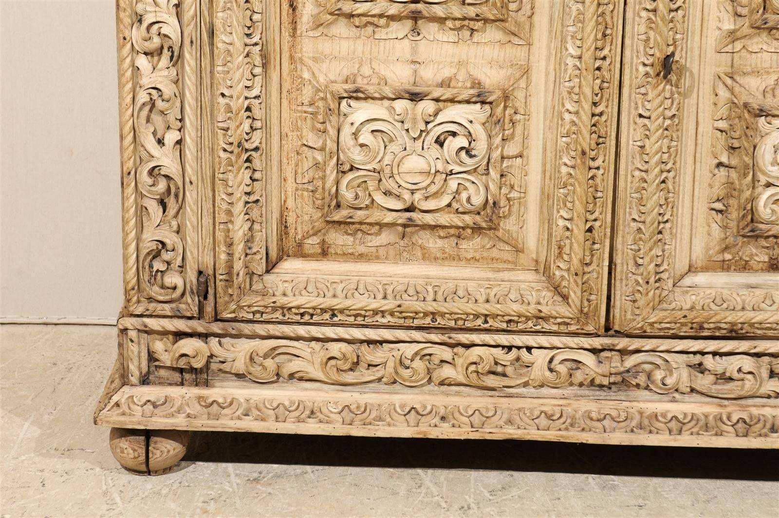 An Italian 18th century two-door credenza with intricate carved details. This bleached Italian buffet is richly carved throughout the front of its body with delicate rinceaux friezes and volute motifs. The doors opens with a key to an inner shelf.