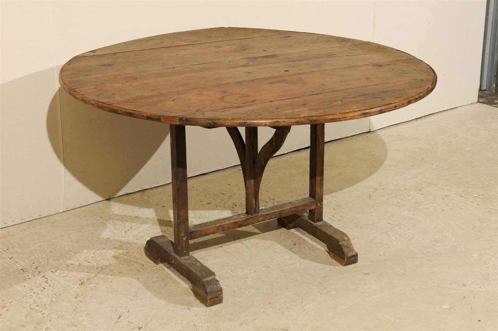 A French wine tasting table with typical tilt-top, from the 20th century. This round French table has some nice wear and patina on the wood top, reflective of age and use. Nice wood grain is also present throughout this piece. The butterfly wedge