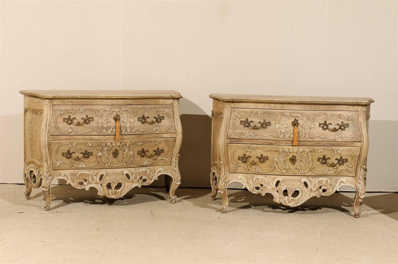 A pair of ashwood Rococo style chests from the late 20th century. This pair of chests features two richly carved drawers with Rococo style pulls and escutcheons. The skirt is scalloped on three sides. The front skirt features a decorated design of