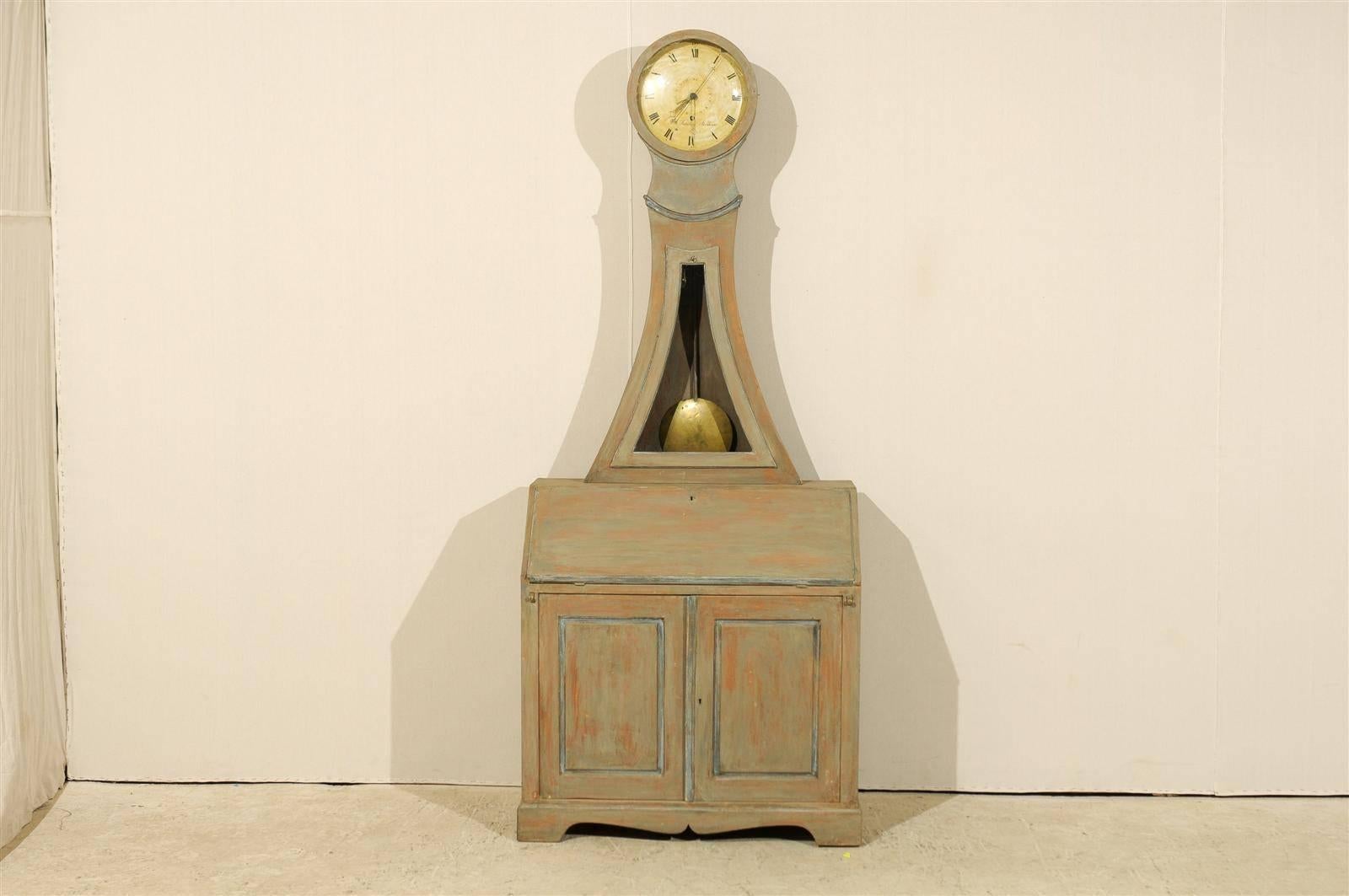 A 19th century Swedish painted wood clock cabinet with slant front desk, circa 1830. The upper clock portion of the piece curves down on both sides, creating a pleasing triangular shape, opening up with a key. The clock portion features a large